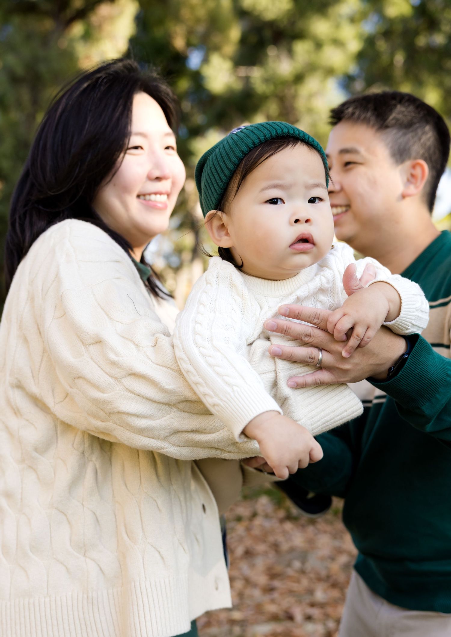 A family wearing white and green sweaters shares playful moments together outdoors on an autumn day.