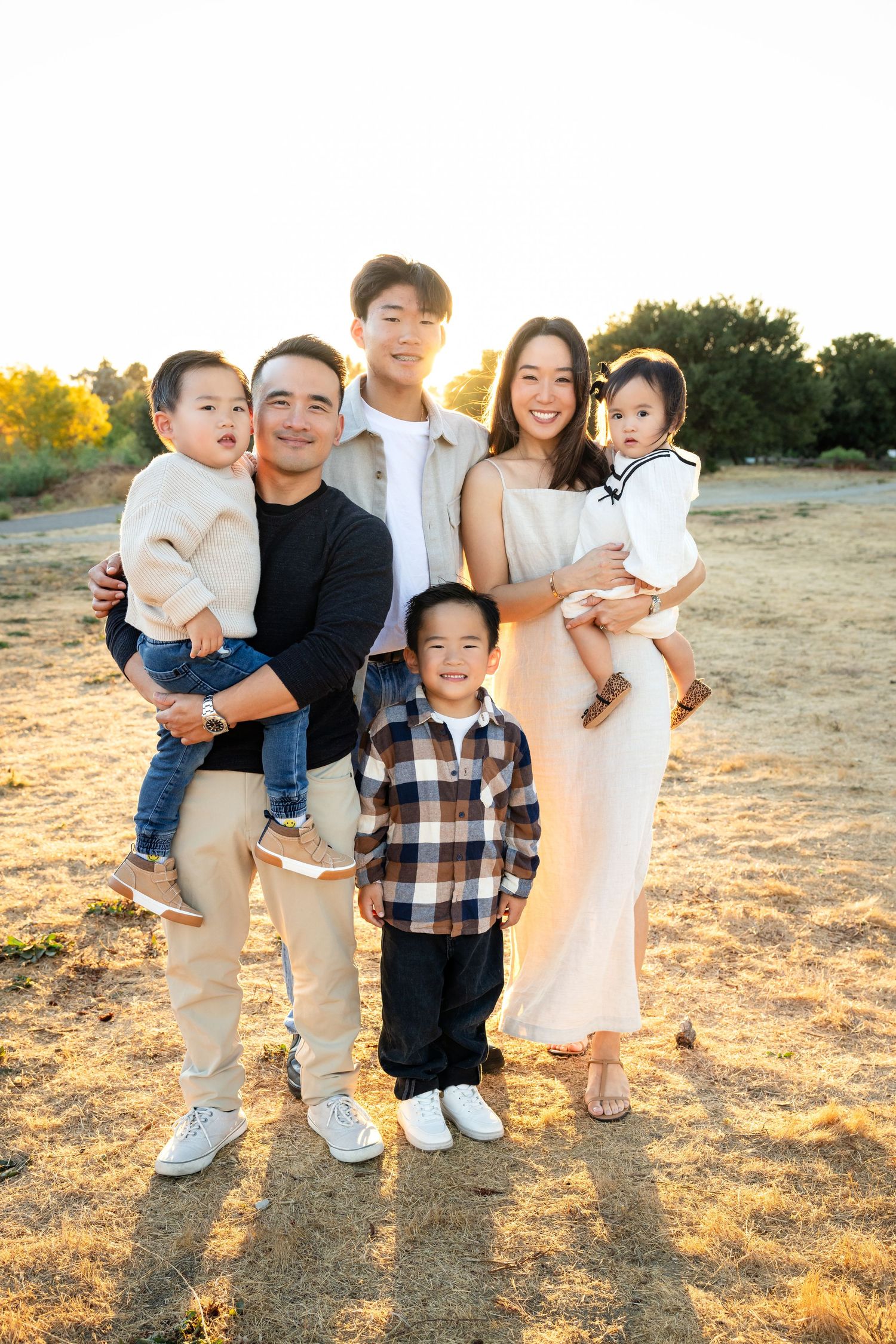 Family standing together on golden grass during sunset photoshoot.