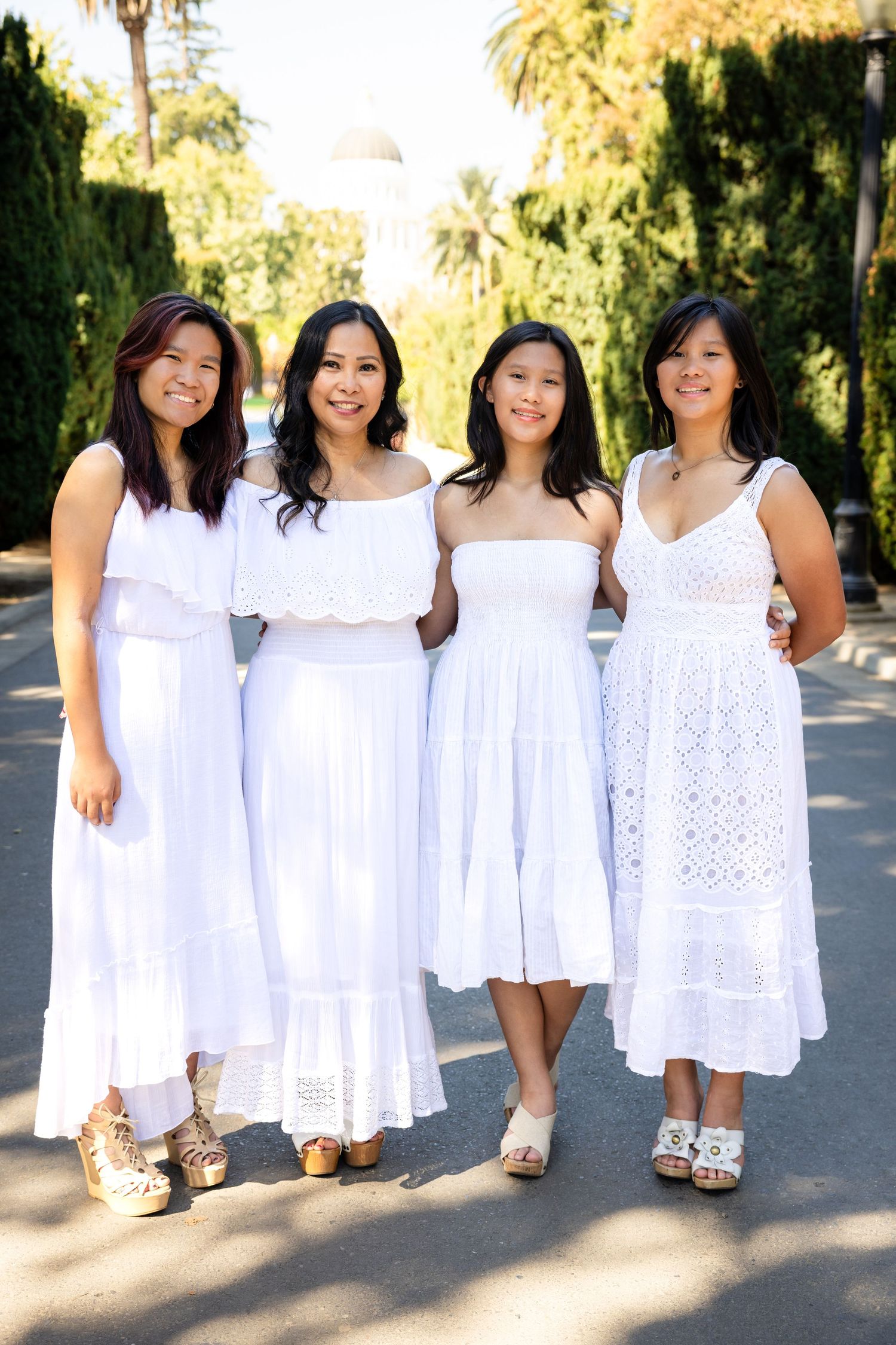 Group photo of women in white summer dresses standing together outdoors in warm sunlight.