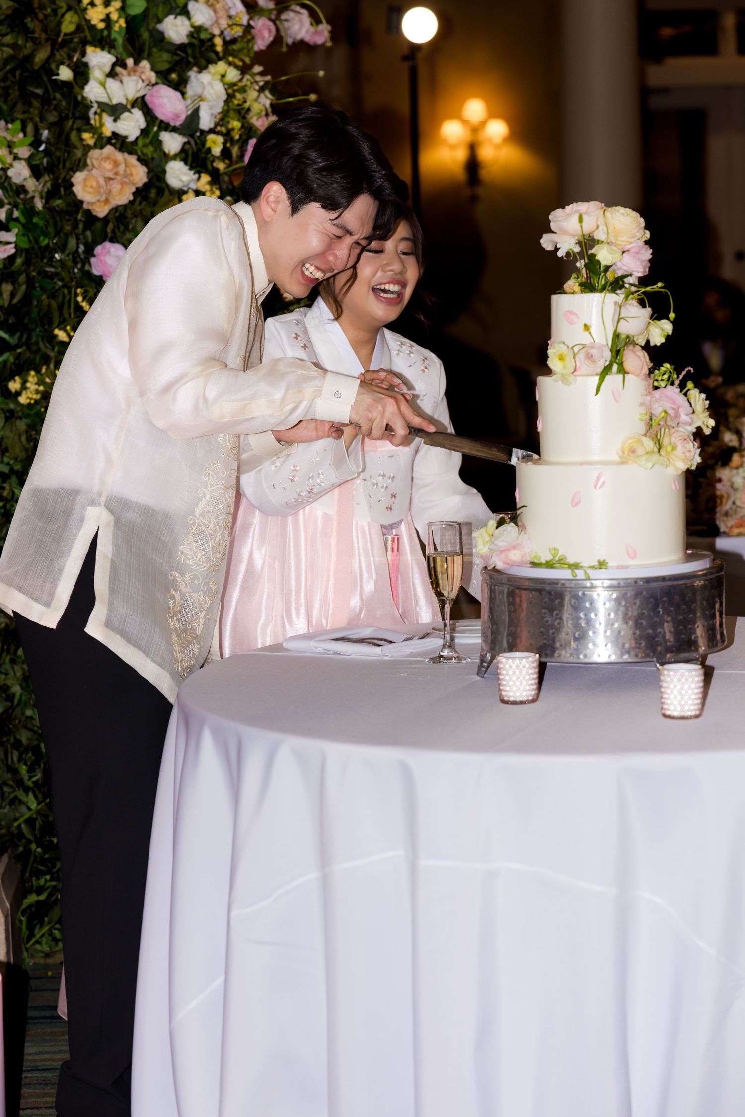 Couple cutting their elegant white wedding cake decorated with fresh flowers.