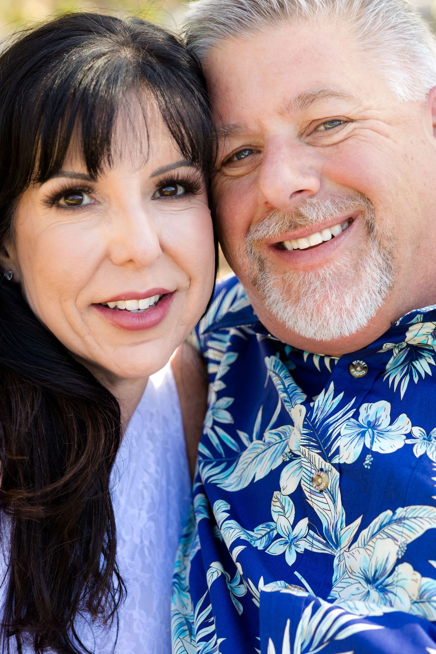 Happy couple taking romantic selfies outdoors with blue floral shirt.