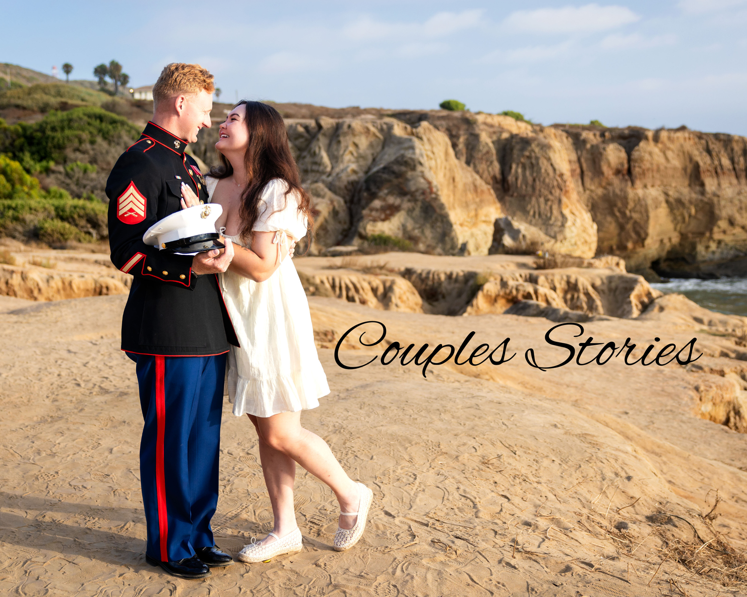 Couple sharing a romantic kiss on a beach, man in Marine dress uniform, woman in white dress, rocky cliffs behind.