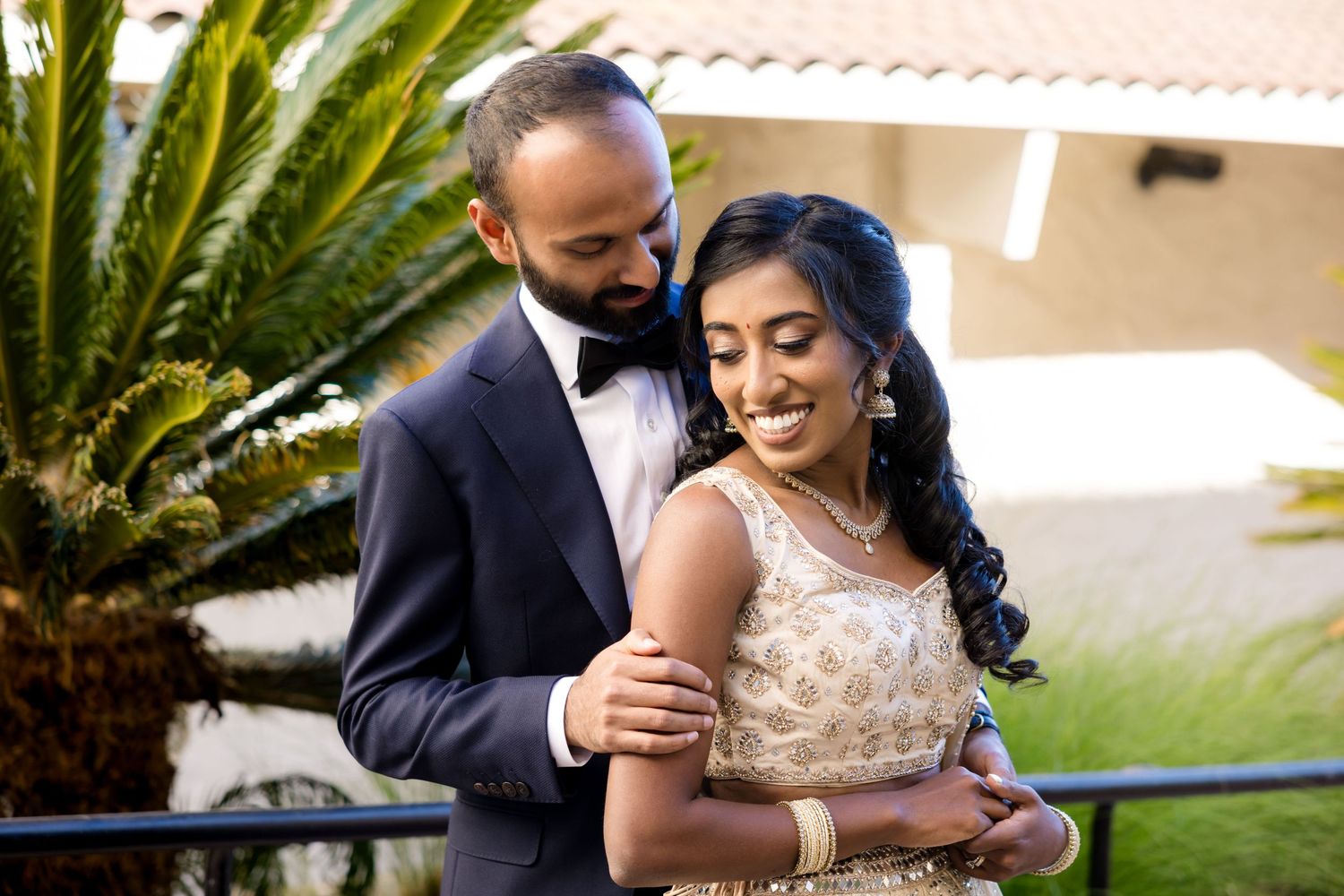 Elegant wedding couple shares intimate moment in garden setting with palm trees.
