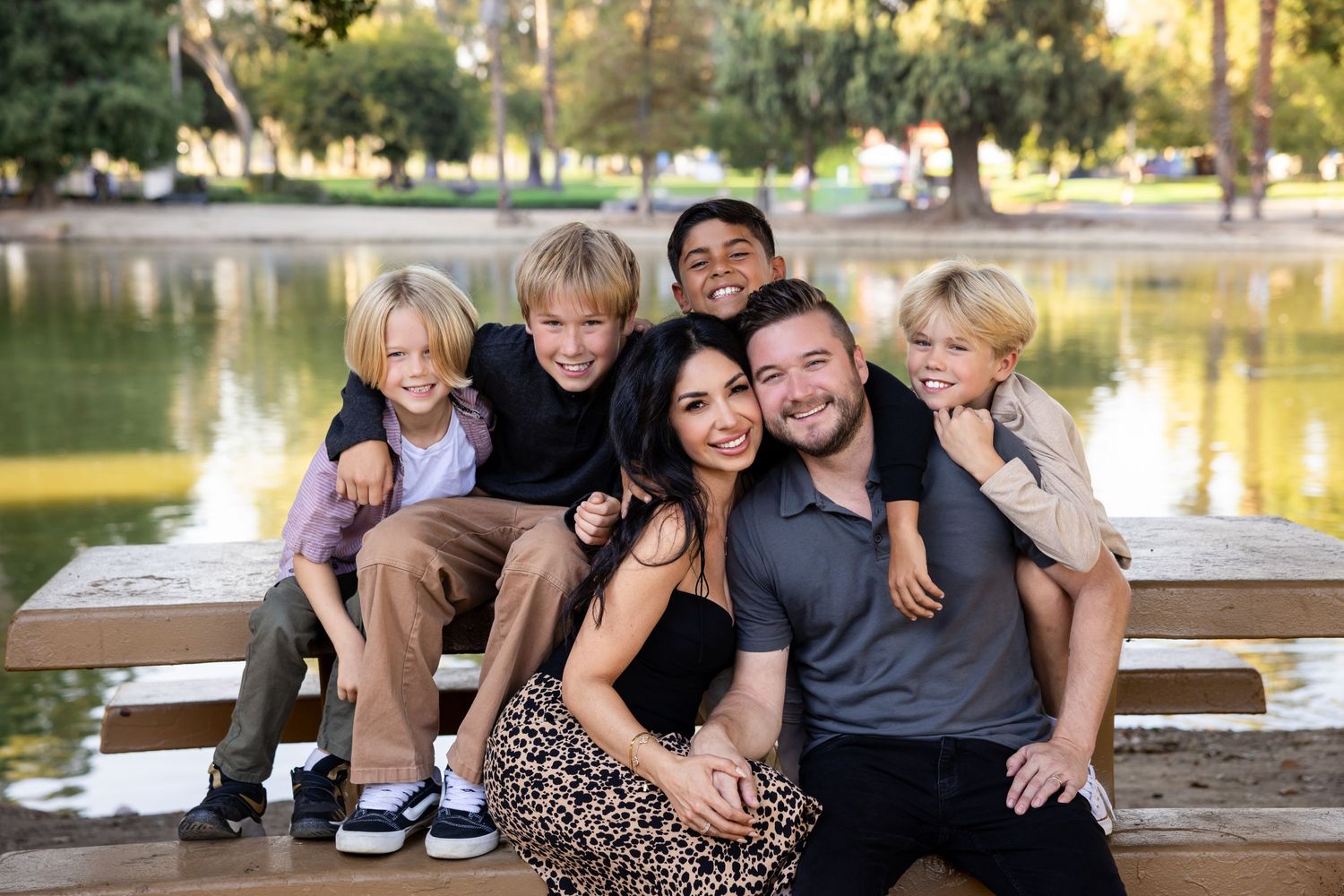 Family group sitting together on wooden dock by a lake at sunset.