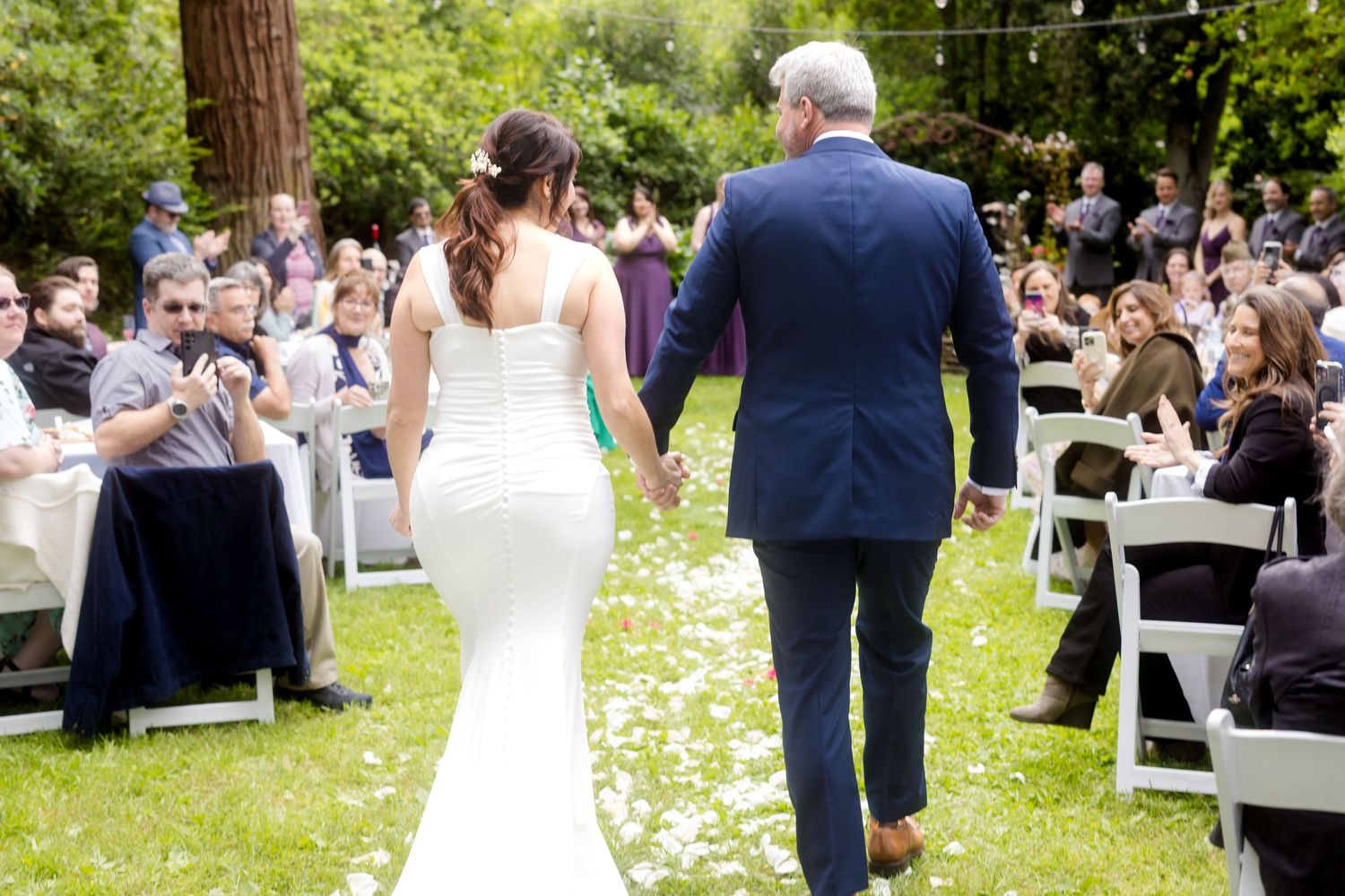 An outdoor wedding reception in a garden setting with white chairs and string lights.