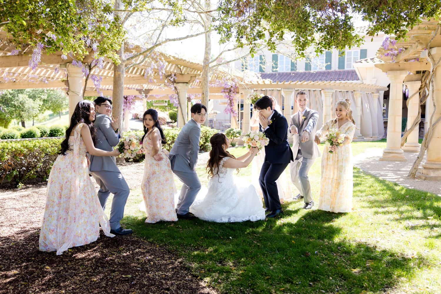 Wedding guests celebrate outdoors under trees at a sunny garden reception.
