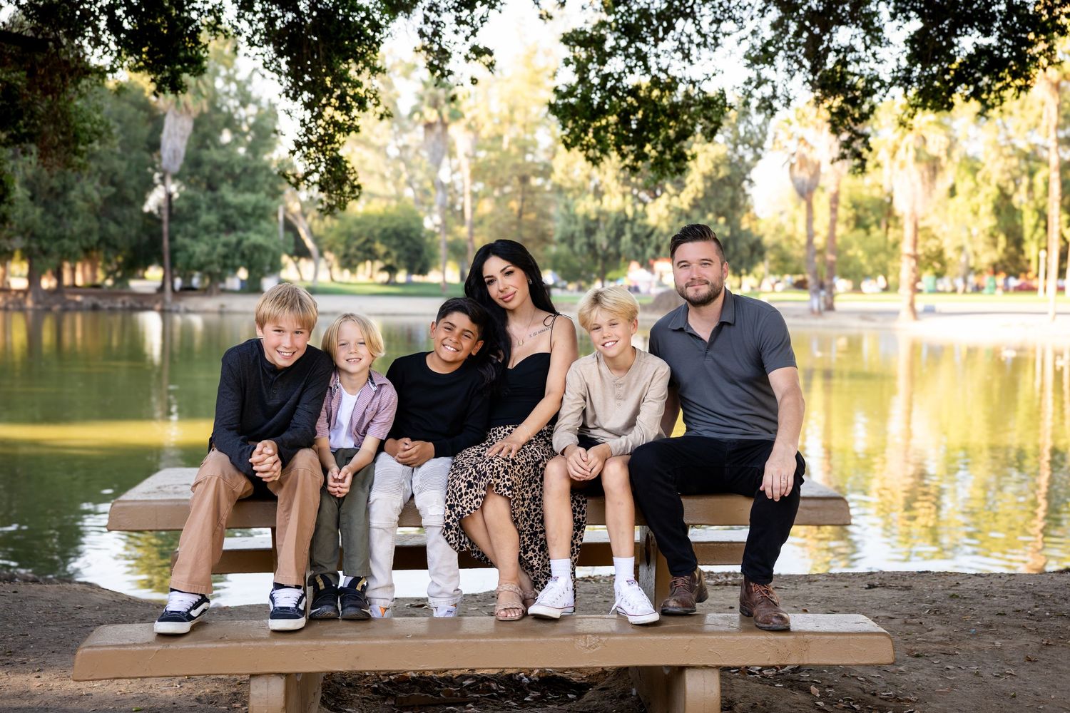 Family sitting together on wooden bench by lake during sunset photo session in park setting.