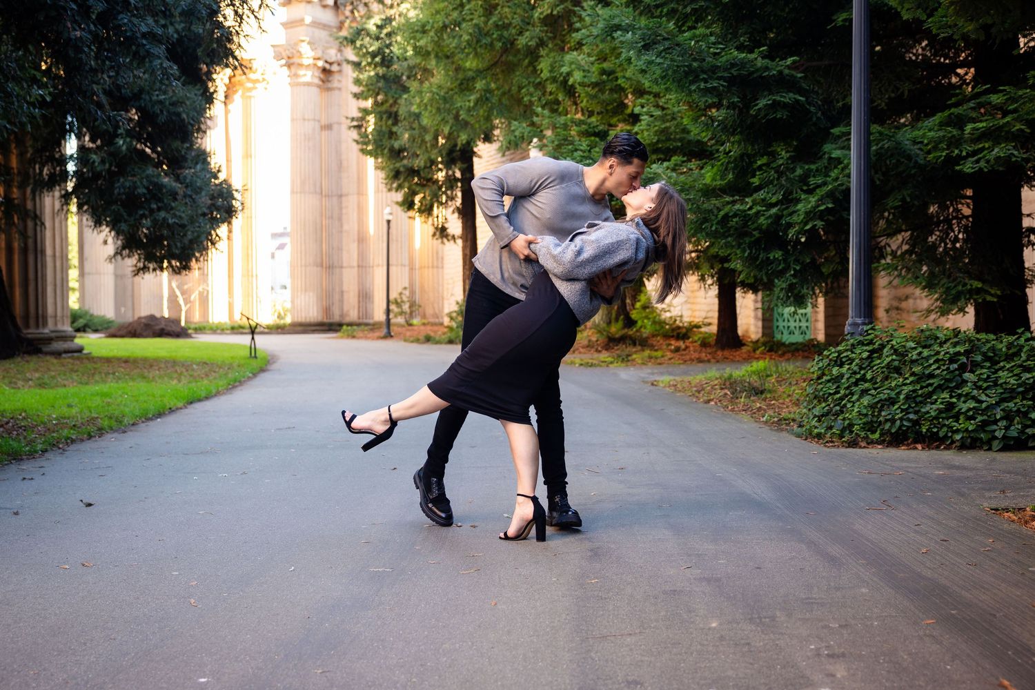 Playful couple dancing and dipping on a tree-lined path.