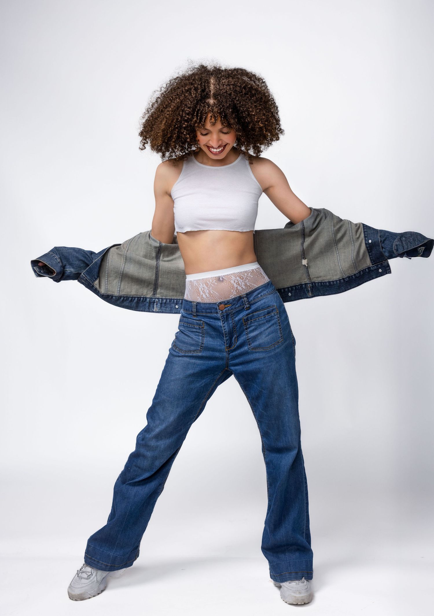 Playful dance movements in baggy denim jeans and white crop top against white background.