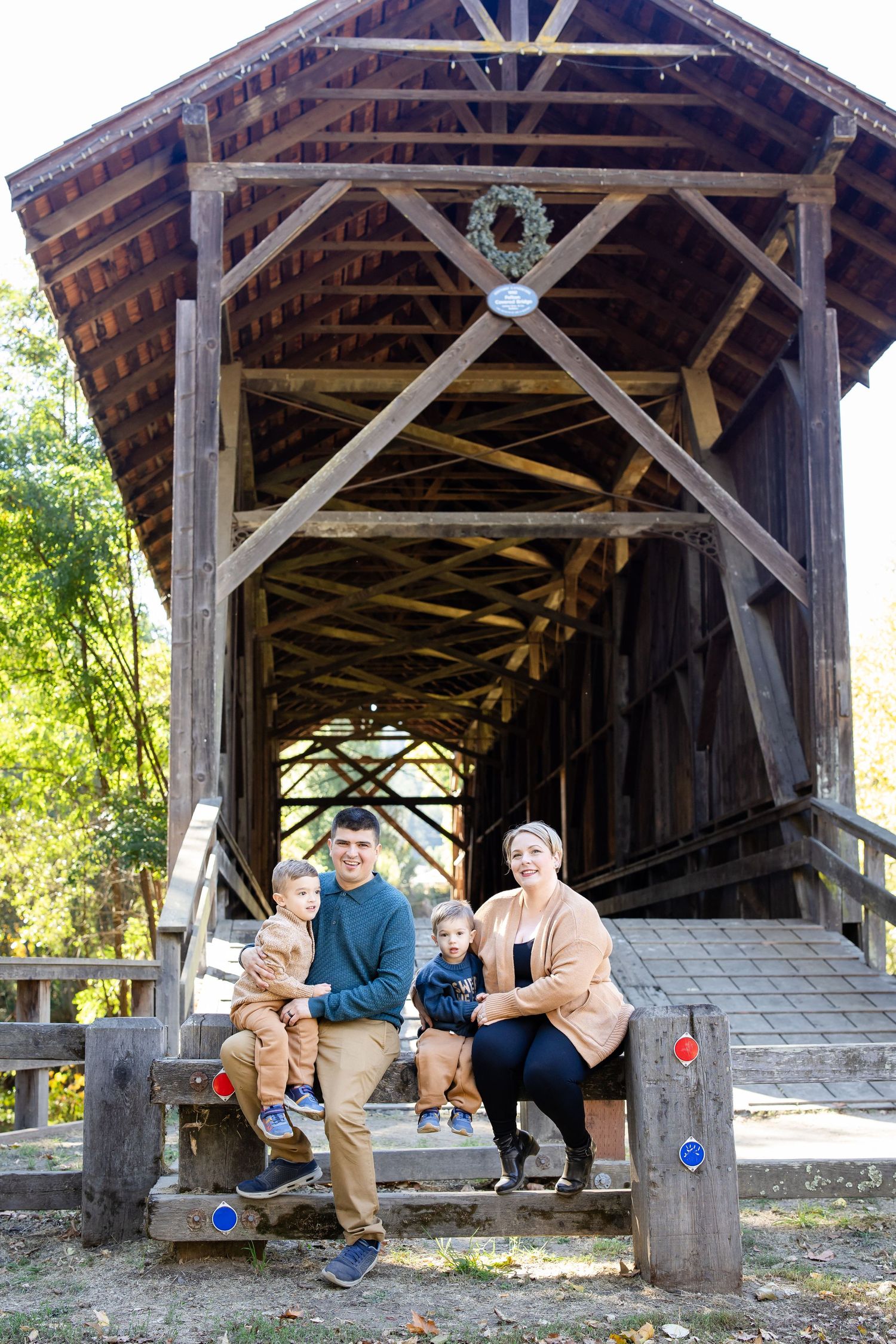 Family poses together inside a rustic wooden covered bridge during an autumn photo session.