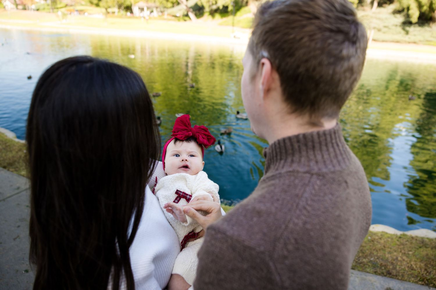 A couple sits close together on a bench near a tranquil pond on a sunny autumn day.