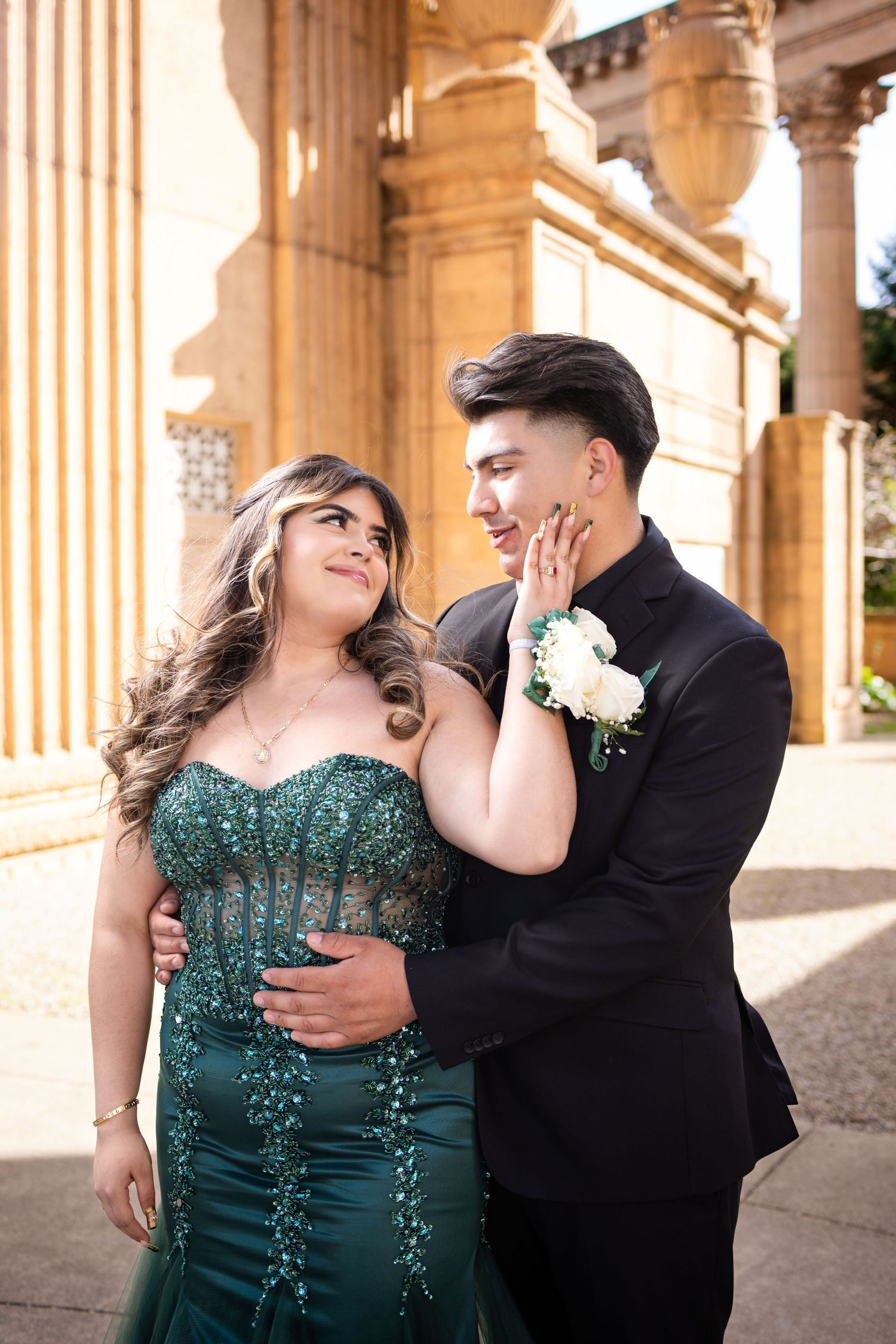 Couple in formal attire dancing and embracing under ornate stone columns at sunset.