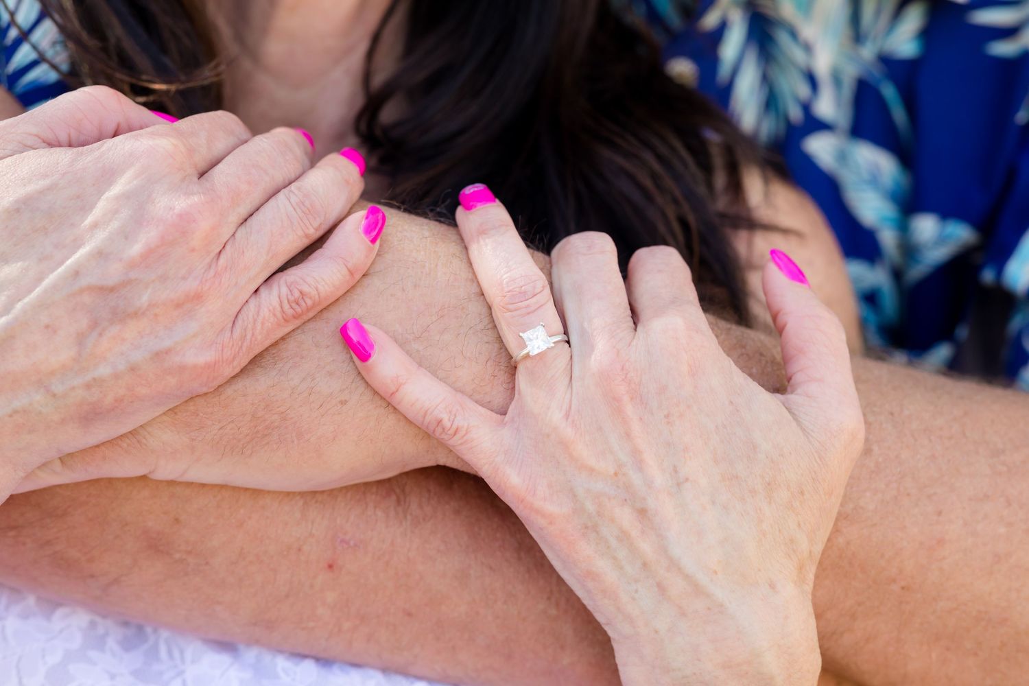 Close-up of hands with engagement ring and pink nail polish.