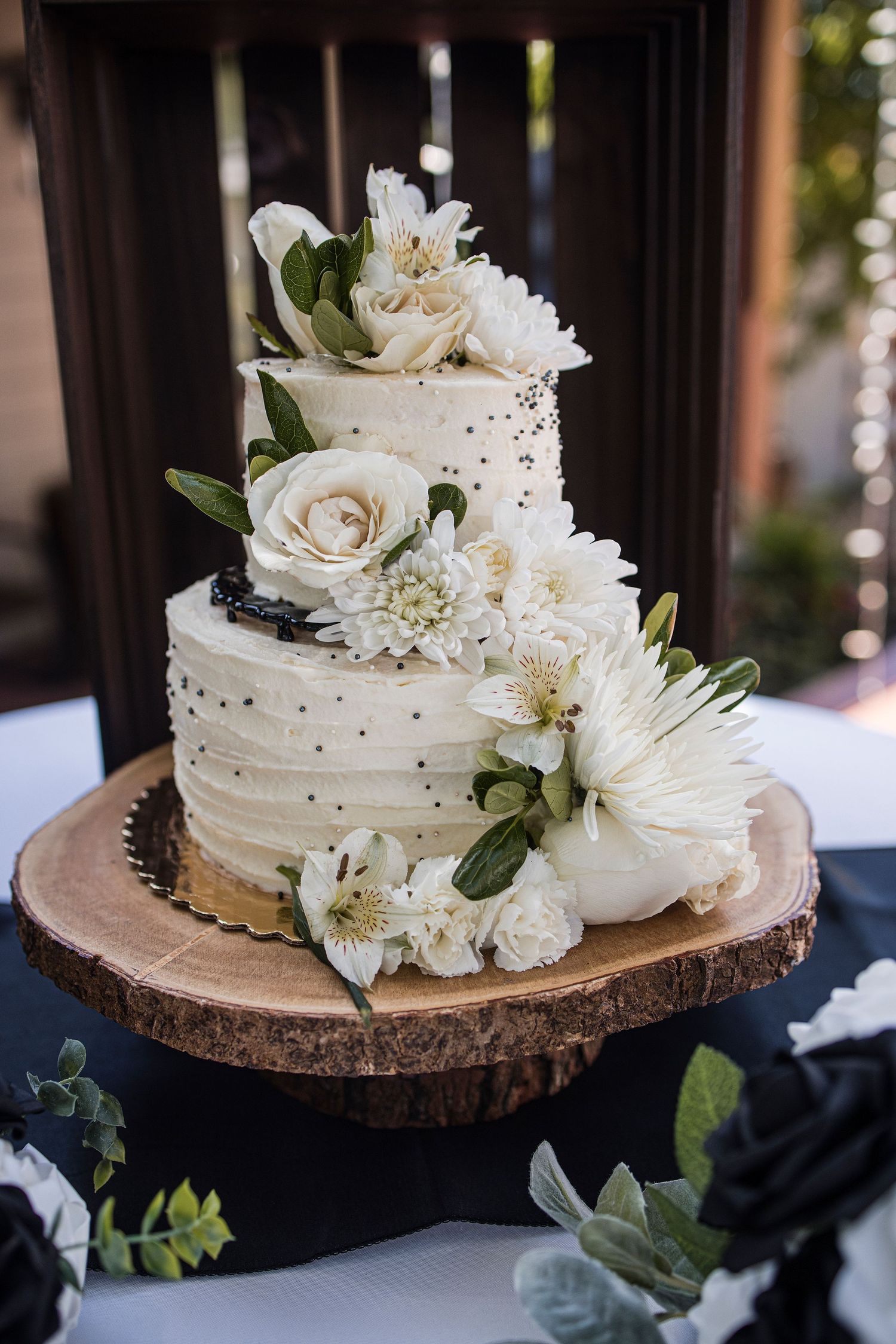 Elegant white wedding cake decorated with roses and flowers on a wooden slice cake stand.