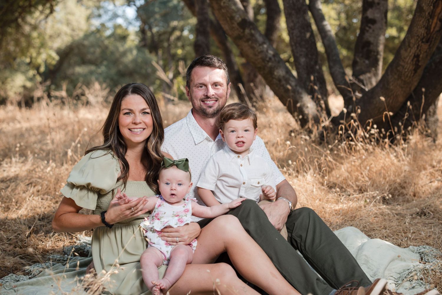 Family sitting together outdoors in a natural setting wearing coordinated neutral colored outfits.