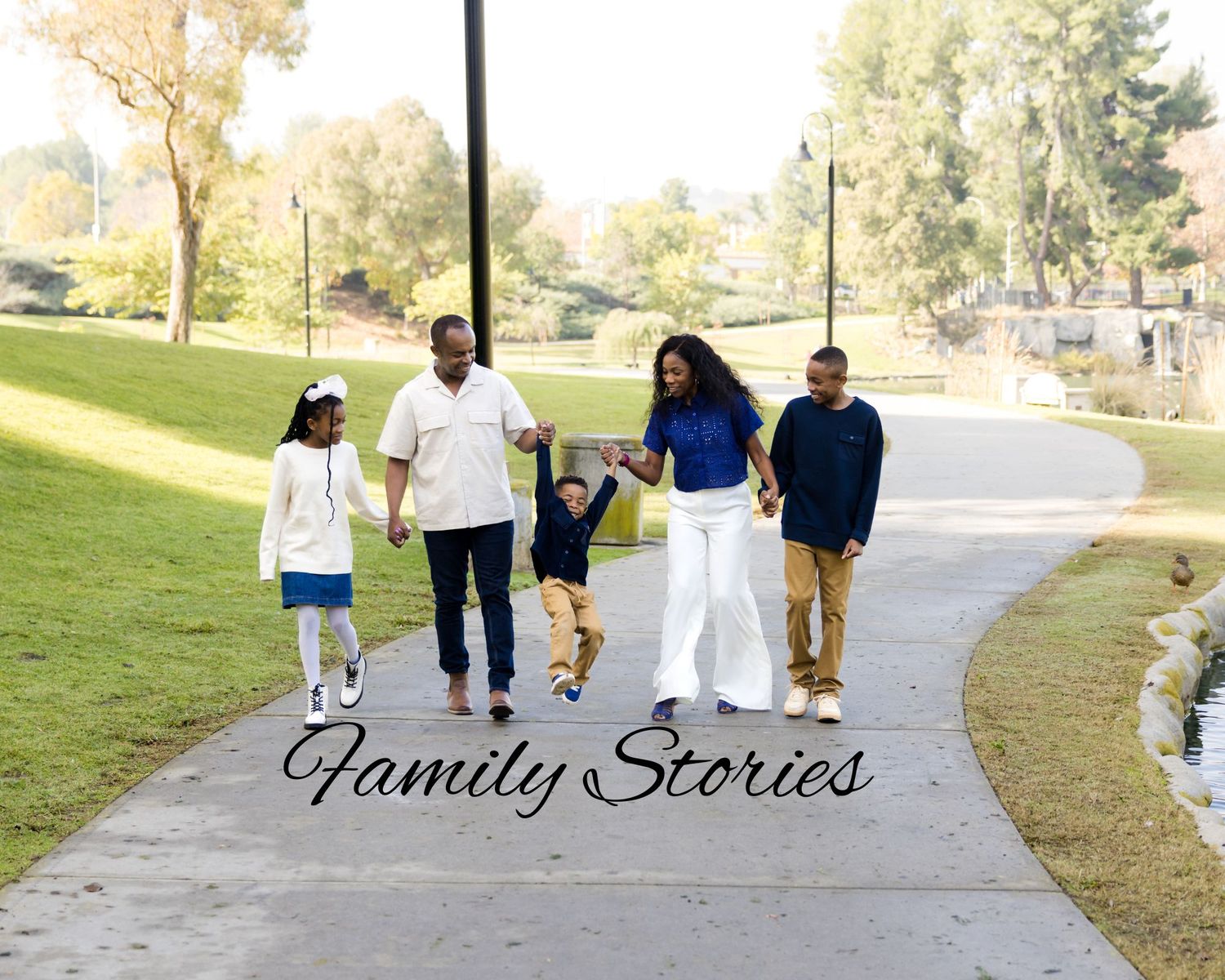 A family walks together holding hands on a paved path through a sunny park on an autumn day.