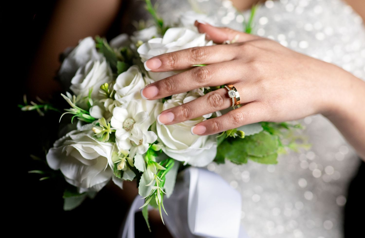Detail shots of bride's hands with wedding ring and white floral bouquet.