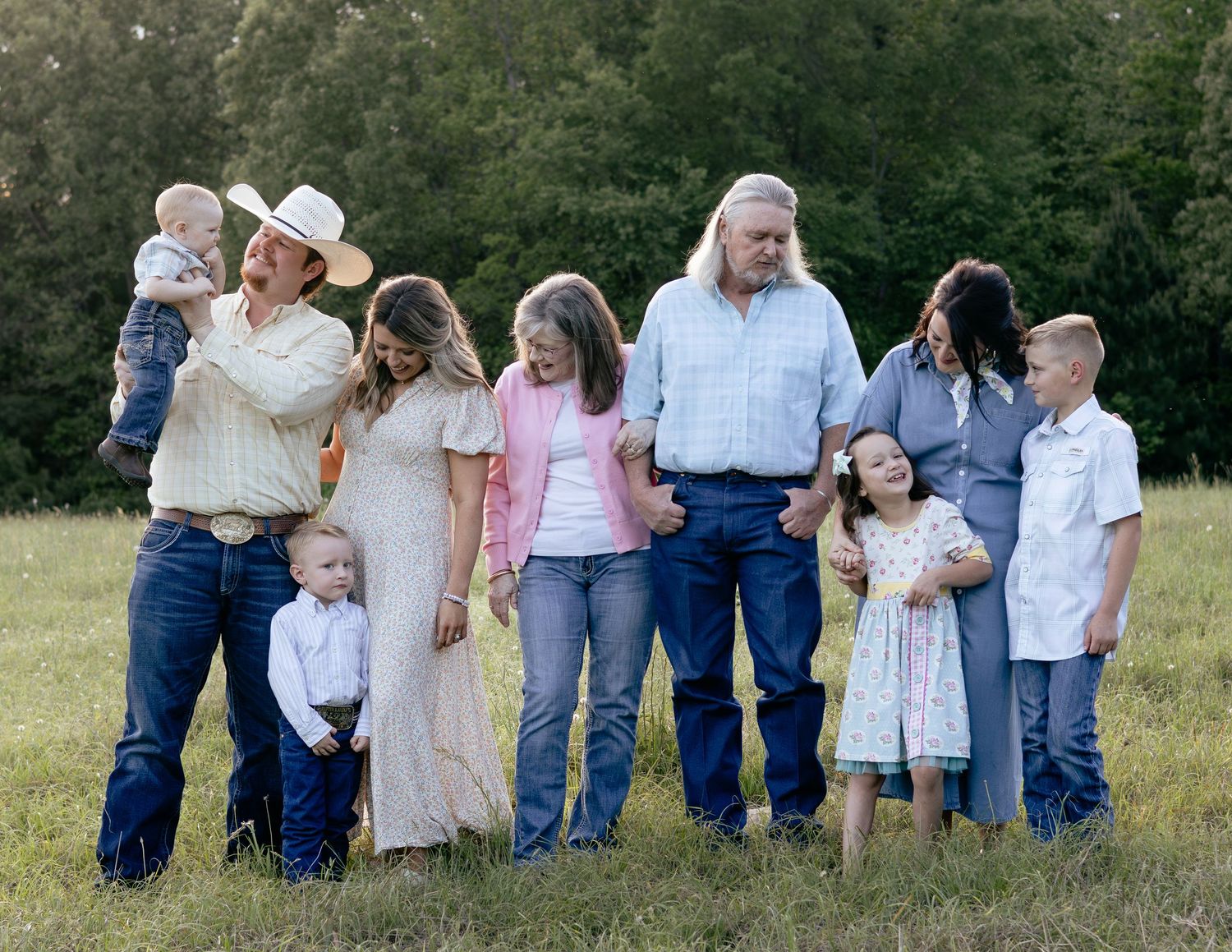 Large family group portrait outdoors in a green field, featuring adults and children in casual country attire.