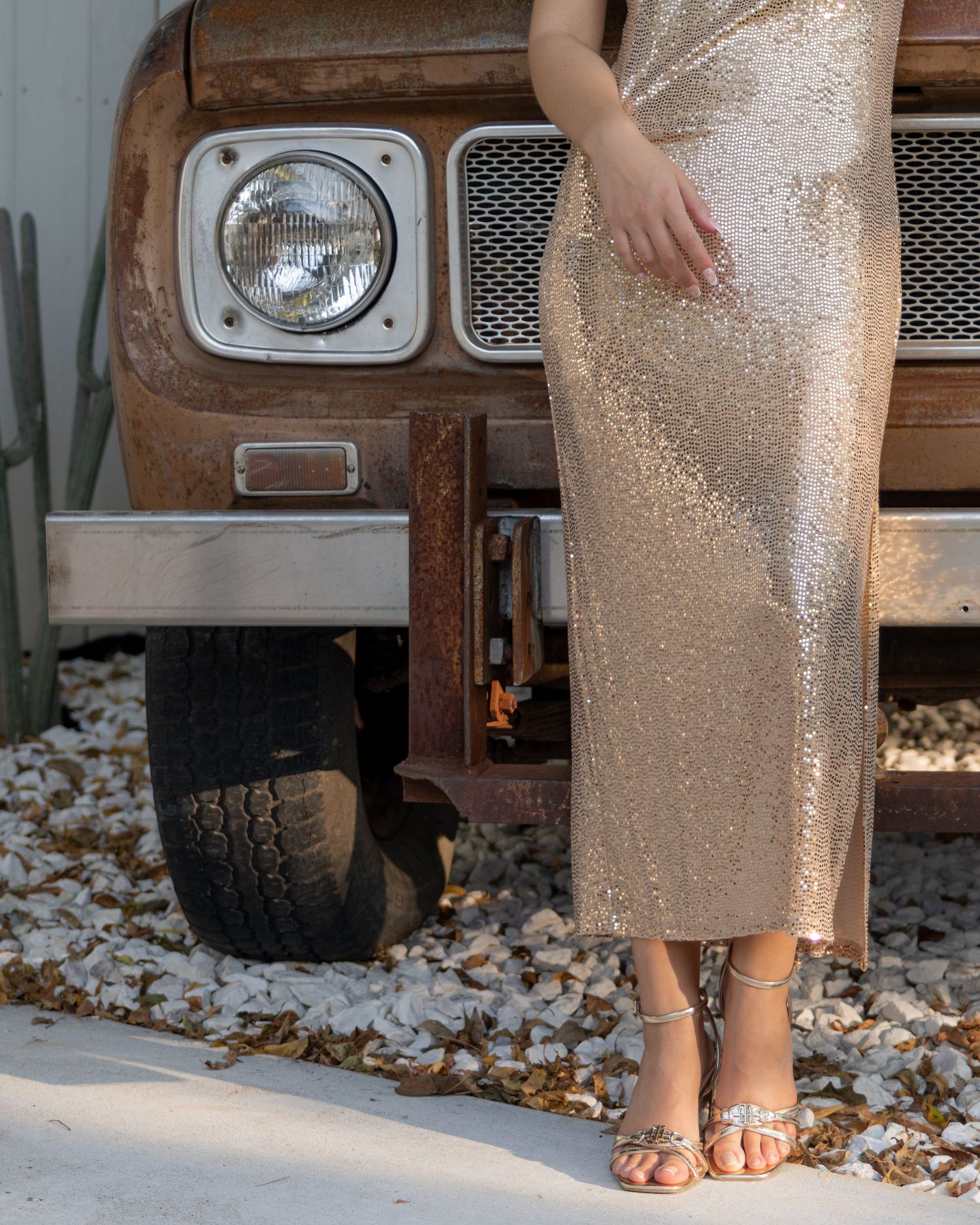 Close-up of gold sequin midi dress and silver strappy heels beside a rustic vintage truck.