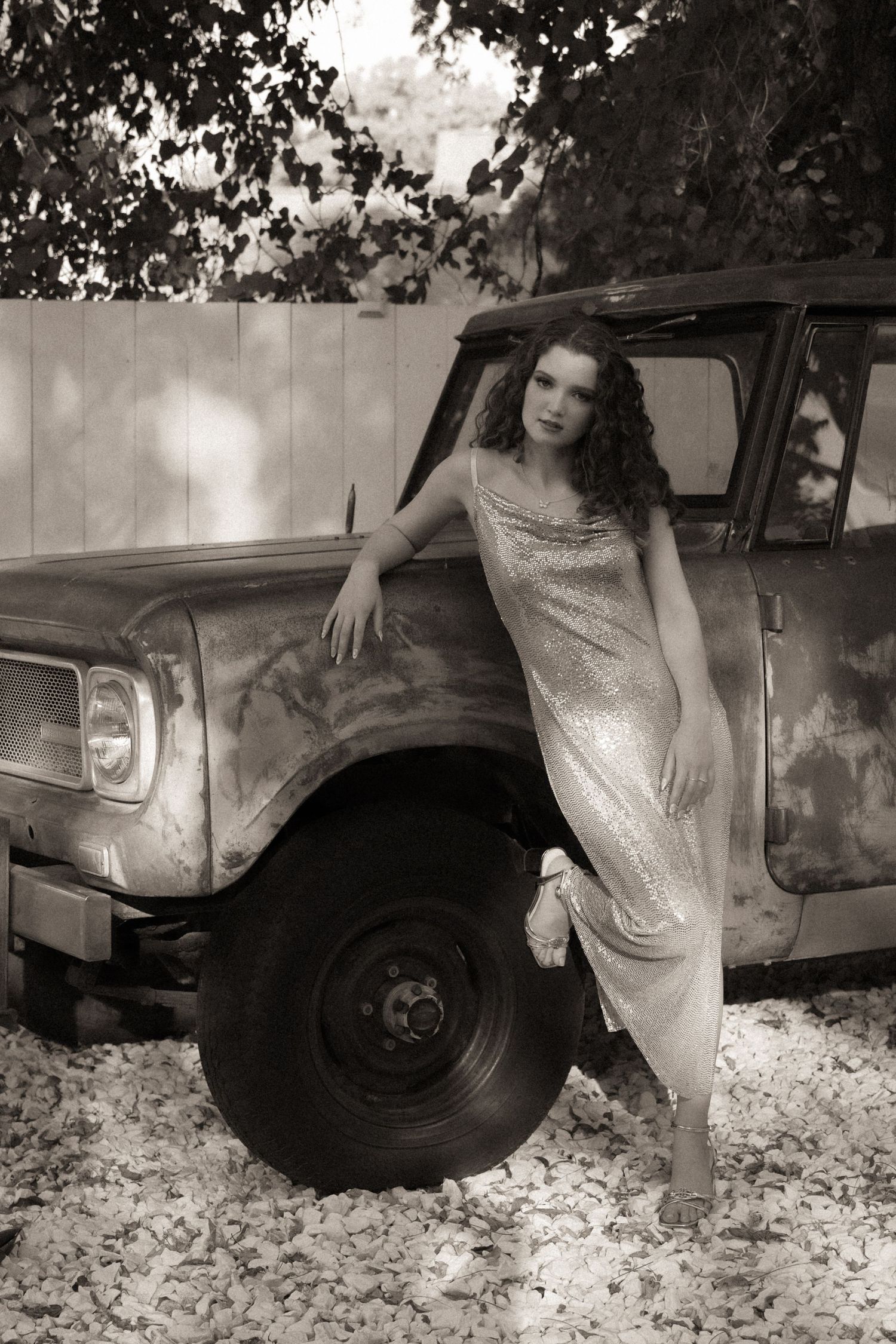 Sepia toned portrait of a woman in gold sequin dress leaning against a rusty vintage truck.