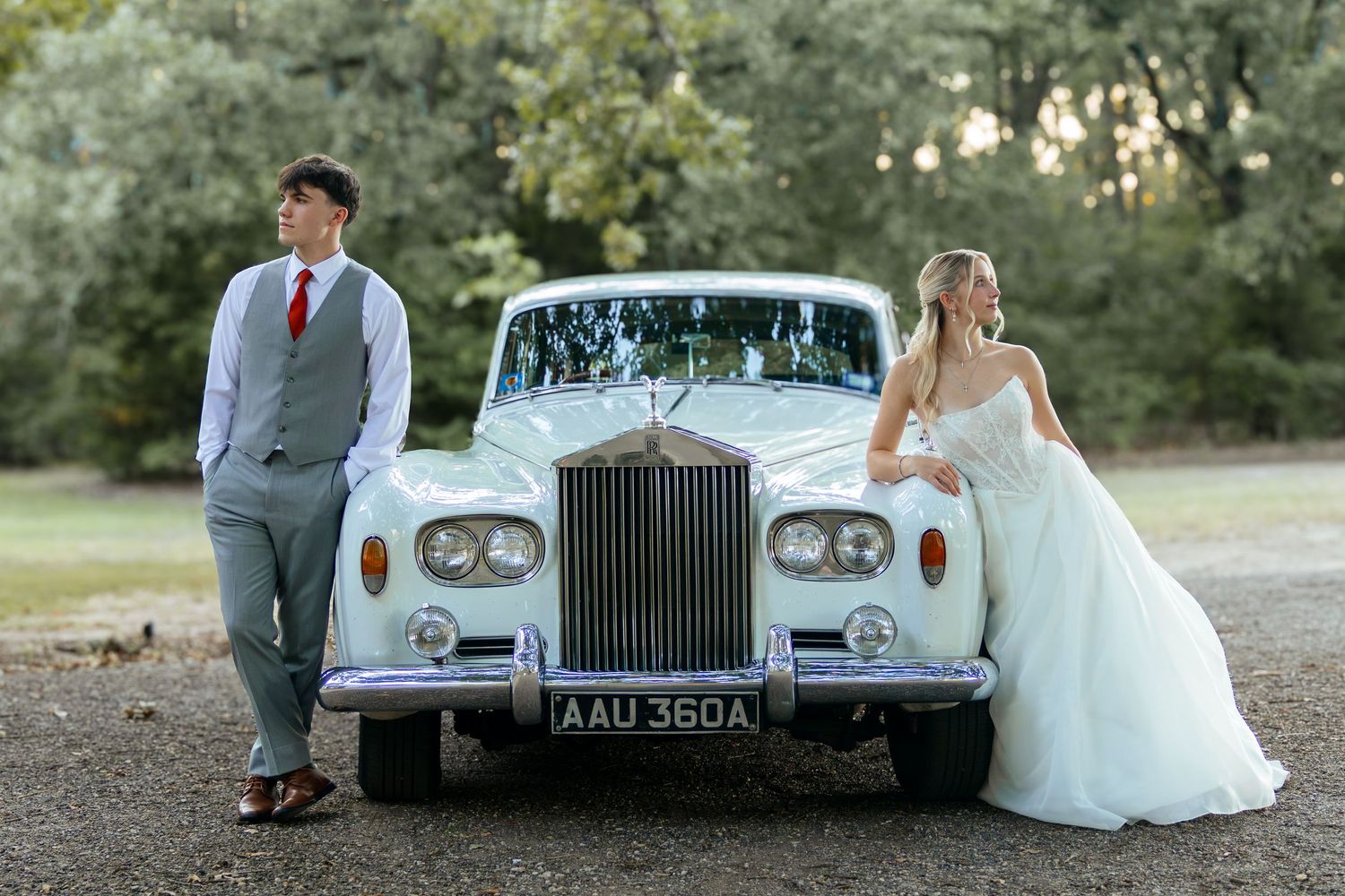 Bride and groom posing beside a classic white Rolls-Royce on their wedding day.