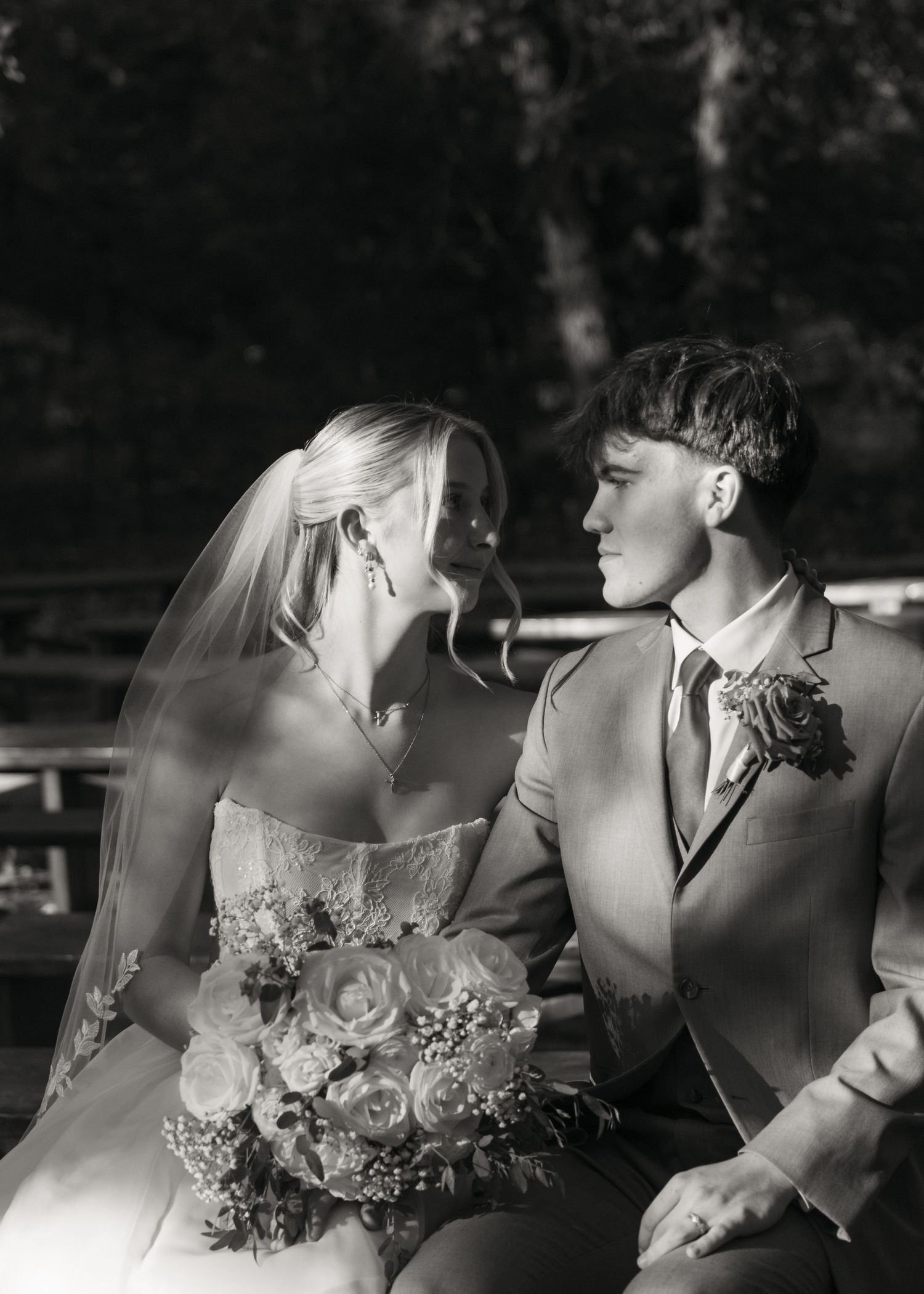 Black and white portrait of bride and groom gazing at each other while seated outdoors on wedding day.