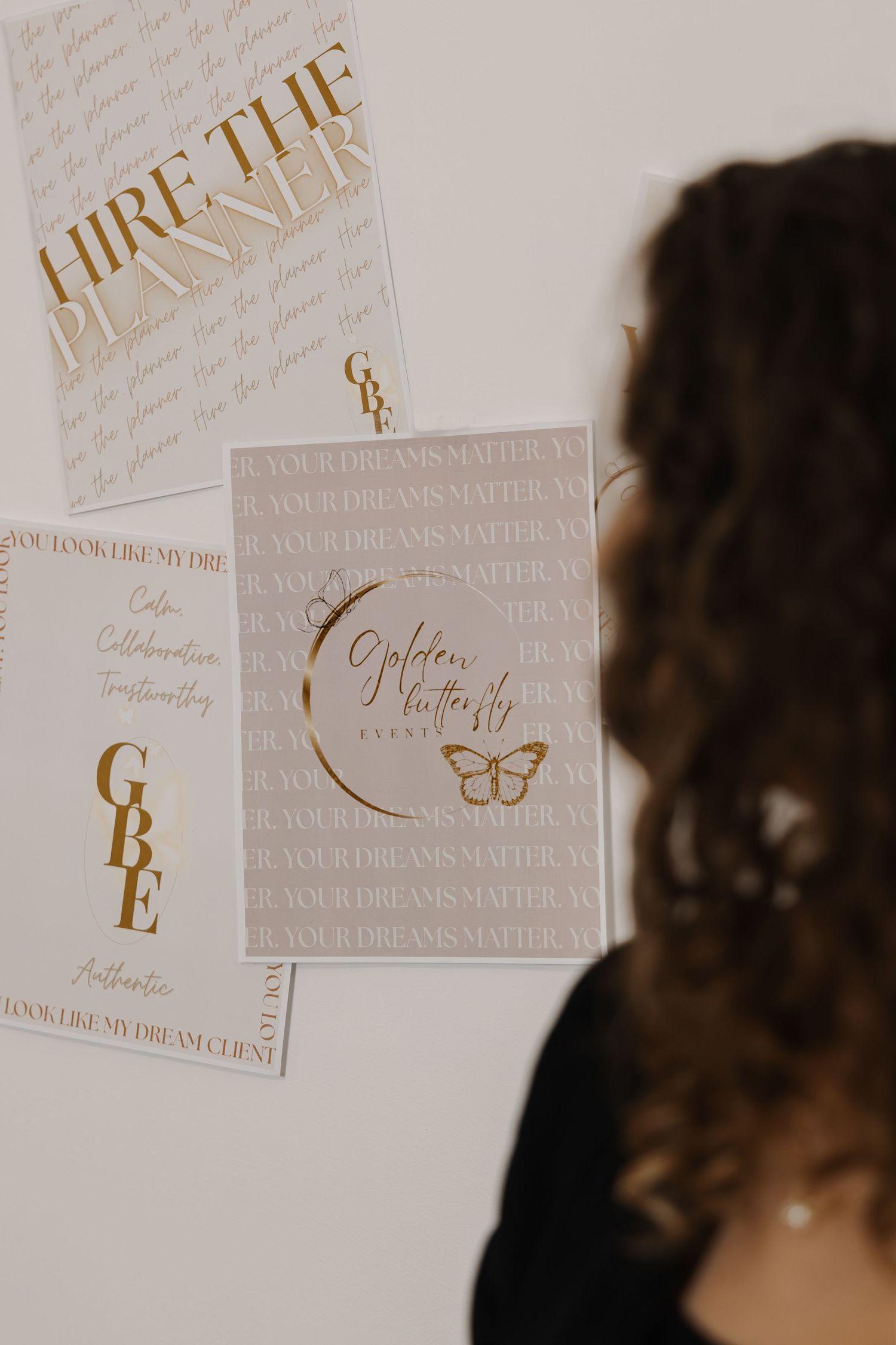 Woman viewing gold and white branding posters for Golden Butterfly Events wedding planning business on a wall.