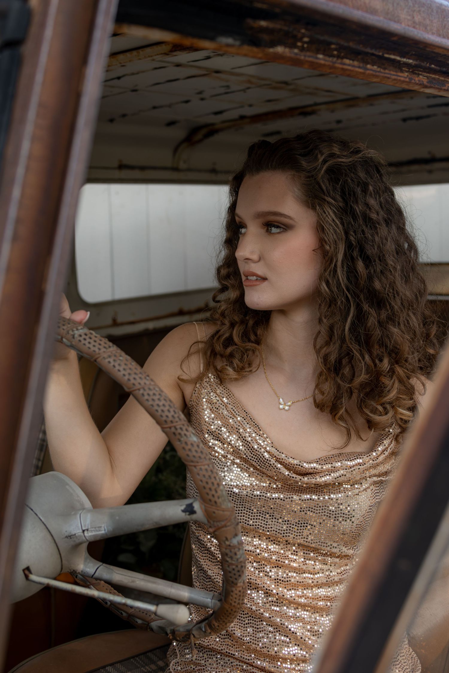 Young woman in gold sequin dress sitting behind steering wheel of vintage rustic truck.