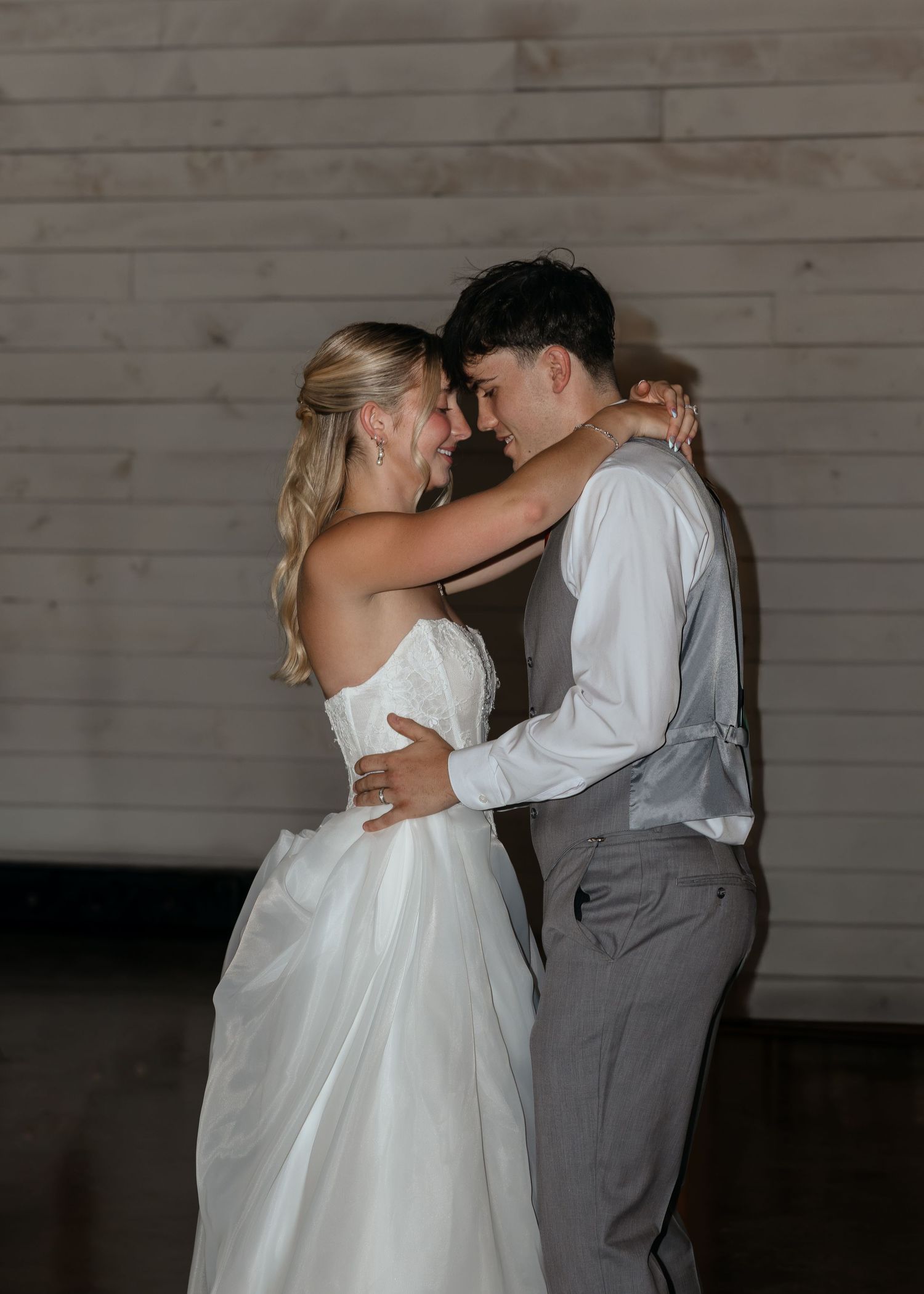 Newlyweds share an intimate first dance moment, bride in white strapless gown and groom in gray vest.