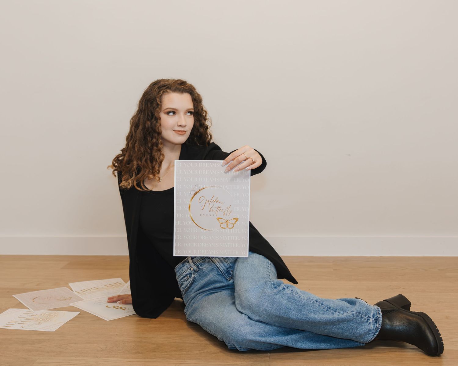 Young woman with curly hair sitting on floor holding elegant gold butterfly logo print design.