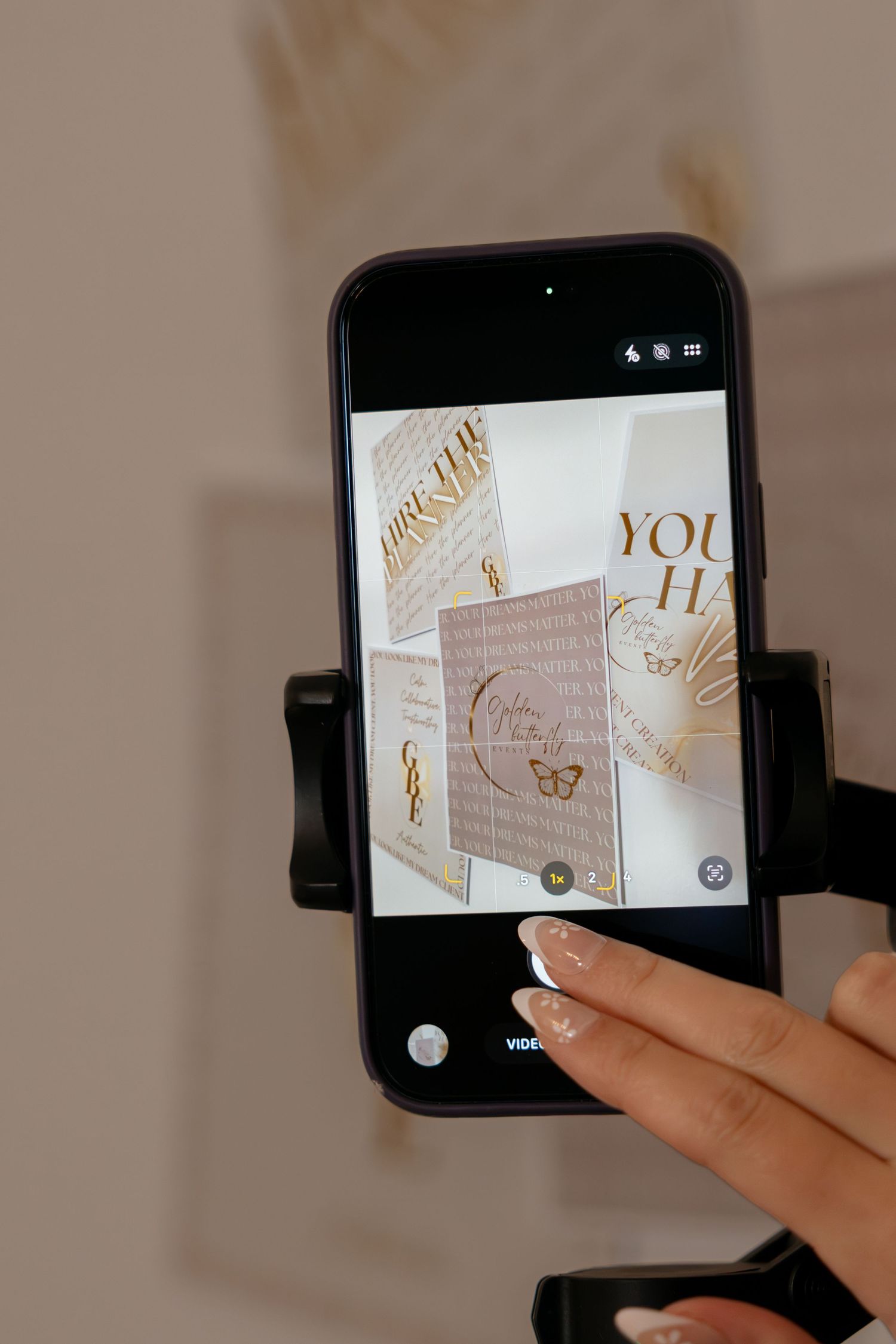 Hand holding a phone on a gimbal photographing gold foil stationery and motivational prints.