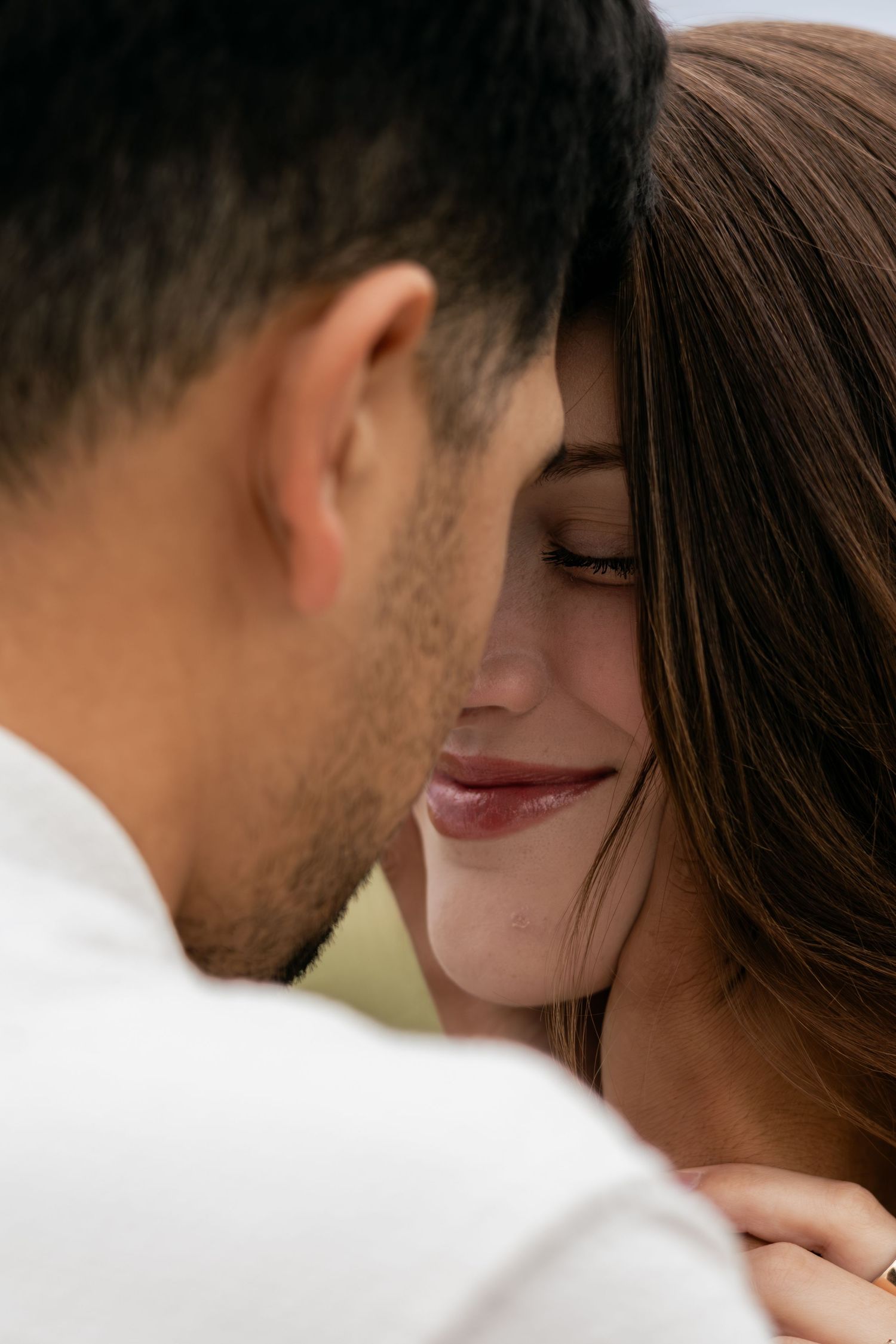 Intimate close-up of couple nearly touching foreheads, woman smiling softly with eyes closed.