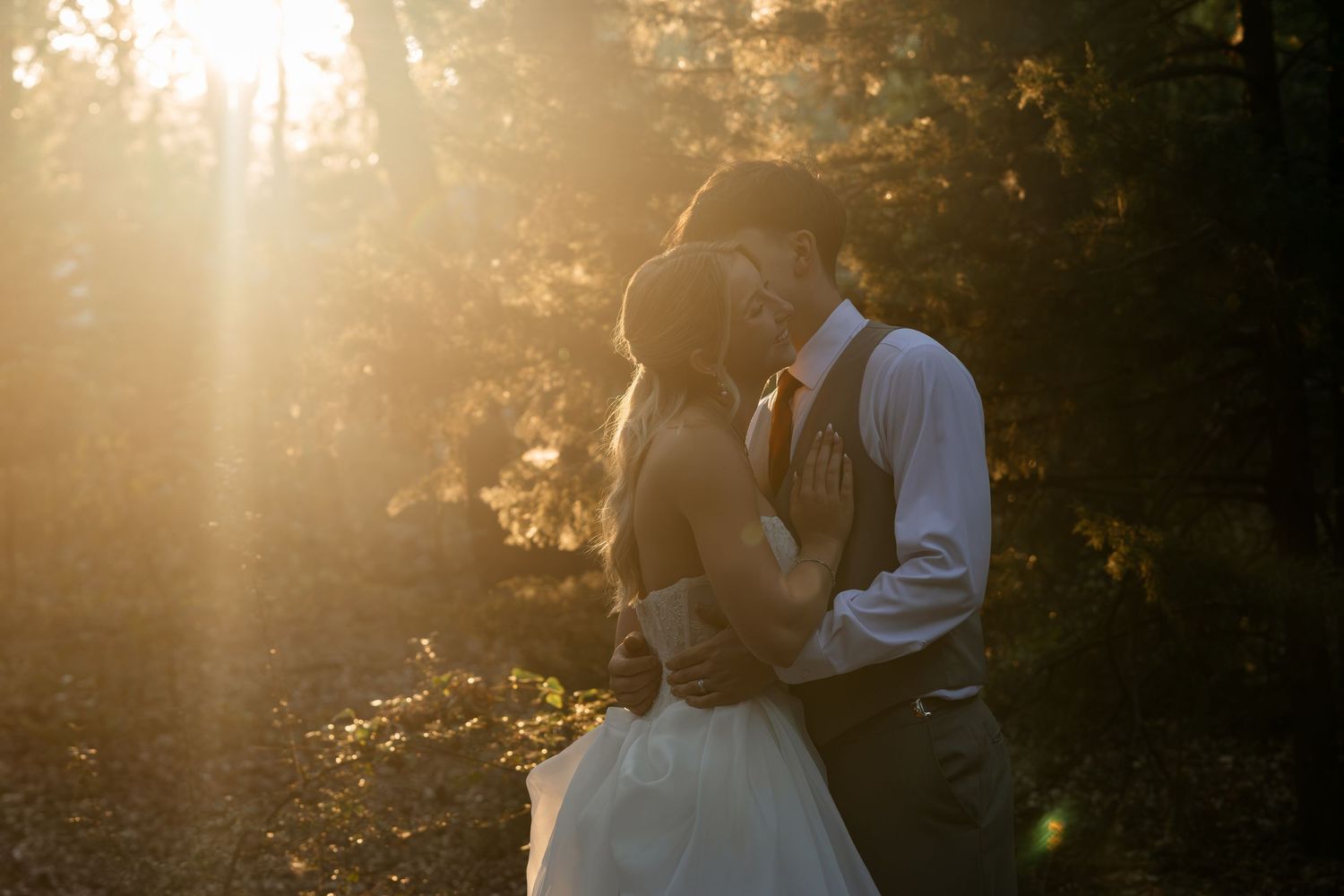 Bride and groom embracing in golden sunset light among autumn trees in a romantic outdoor wedding portrait.