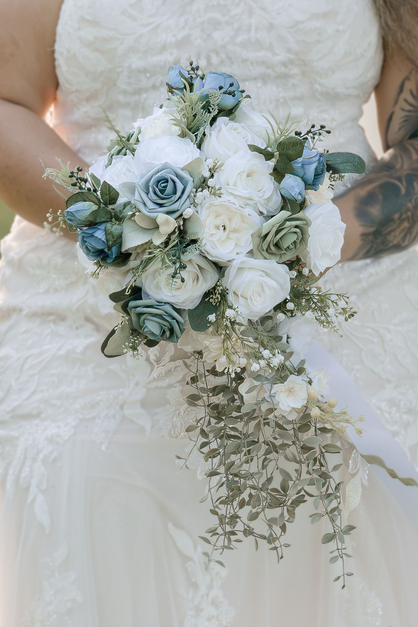 Bride holding cascading wedding bouquet with dusty blue and white roses, eucalyptus greenery, in lace wedding dress.