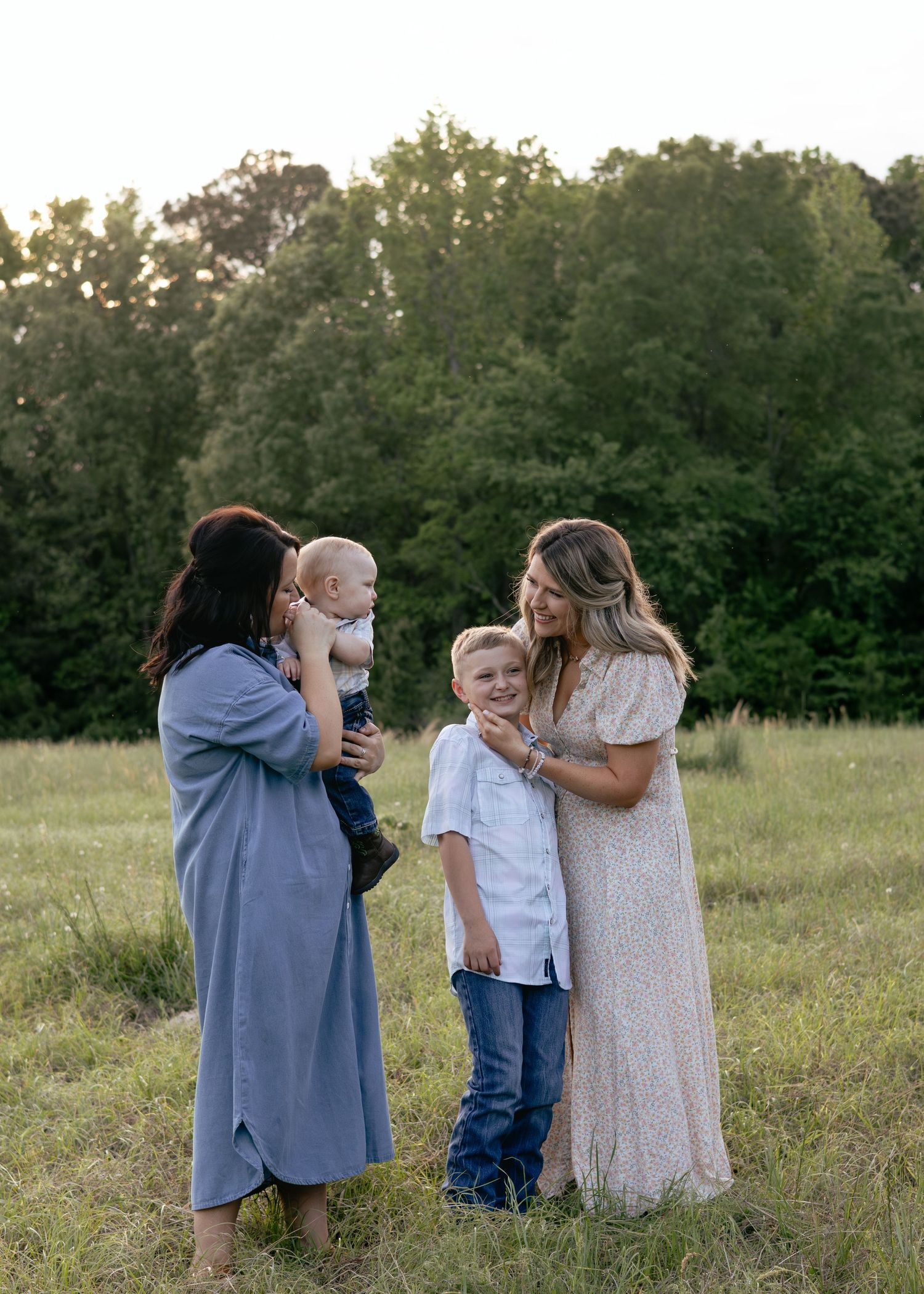 Two women with children share a joyful moment in a green meadow during golden hour.