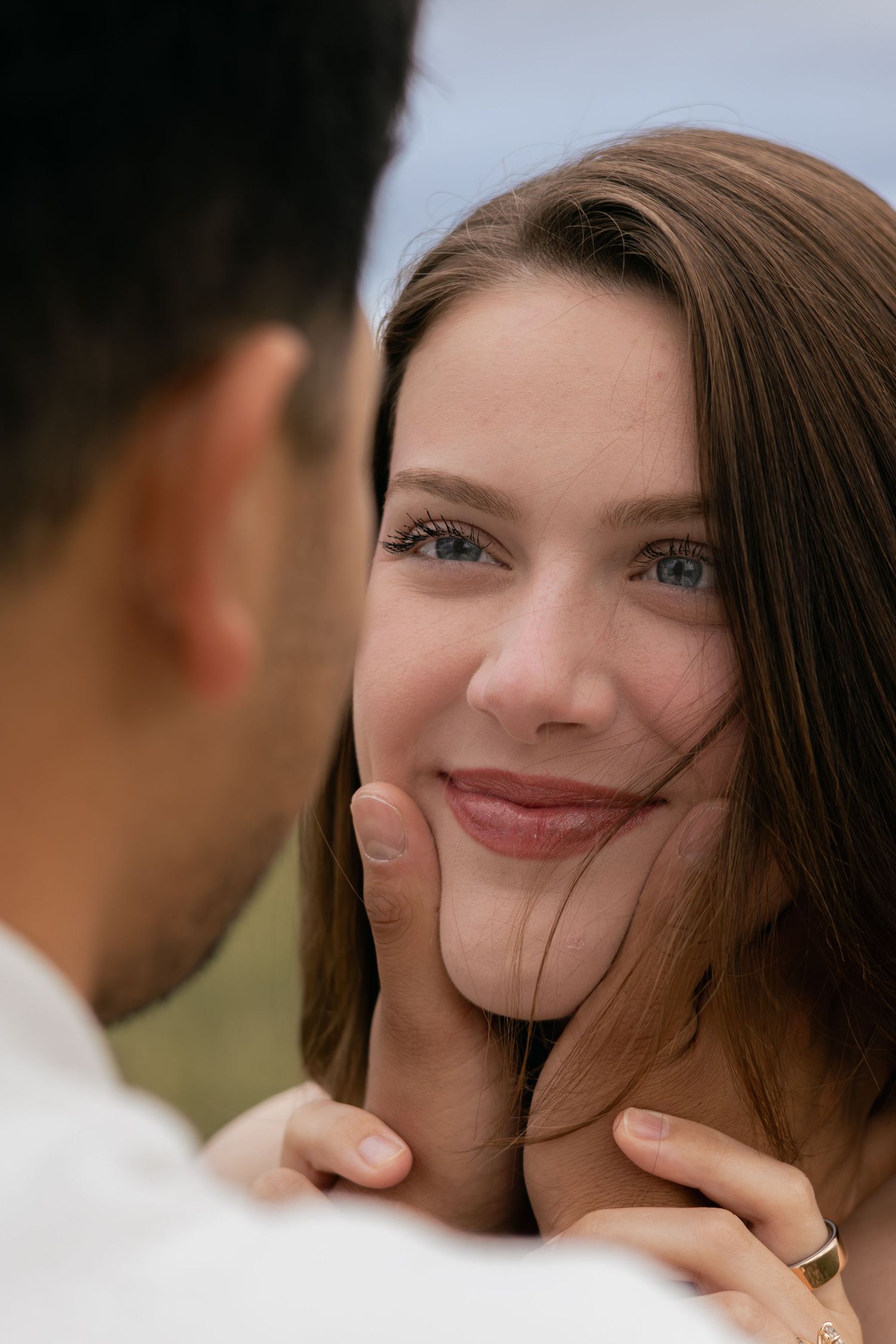 Close-up of smiling woman with blue eyes, man gently cupping her face outdoors.