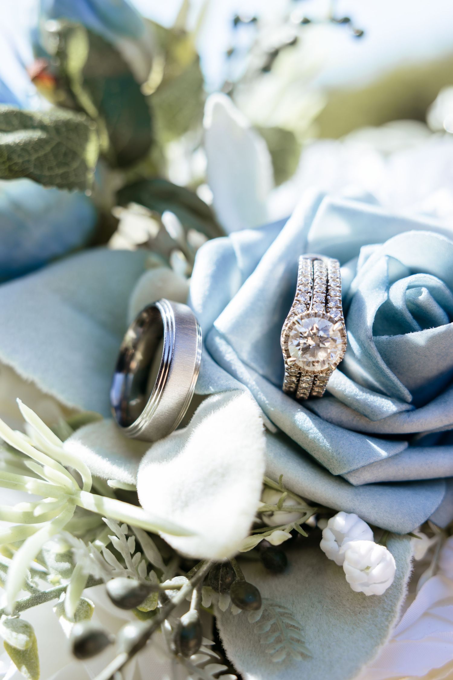 Diamond engagement ring and wedding band resting on a dusty blue rose bouquet with silver foliage.