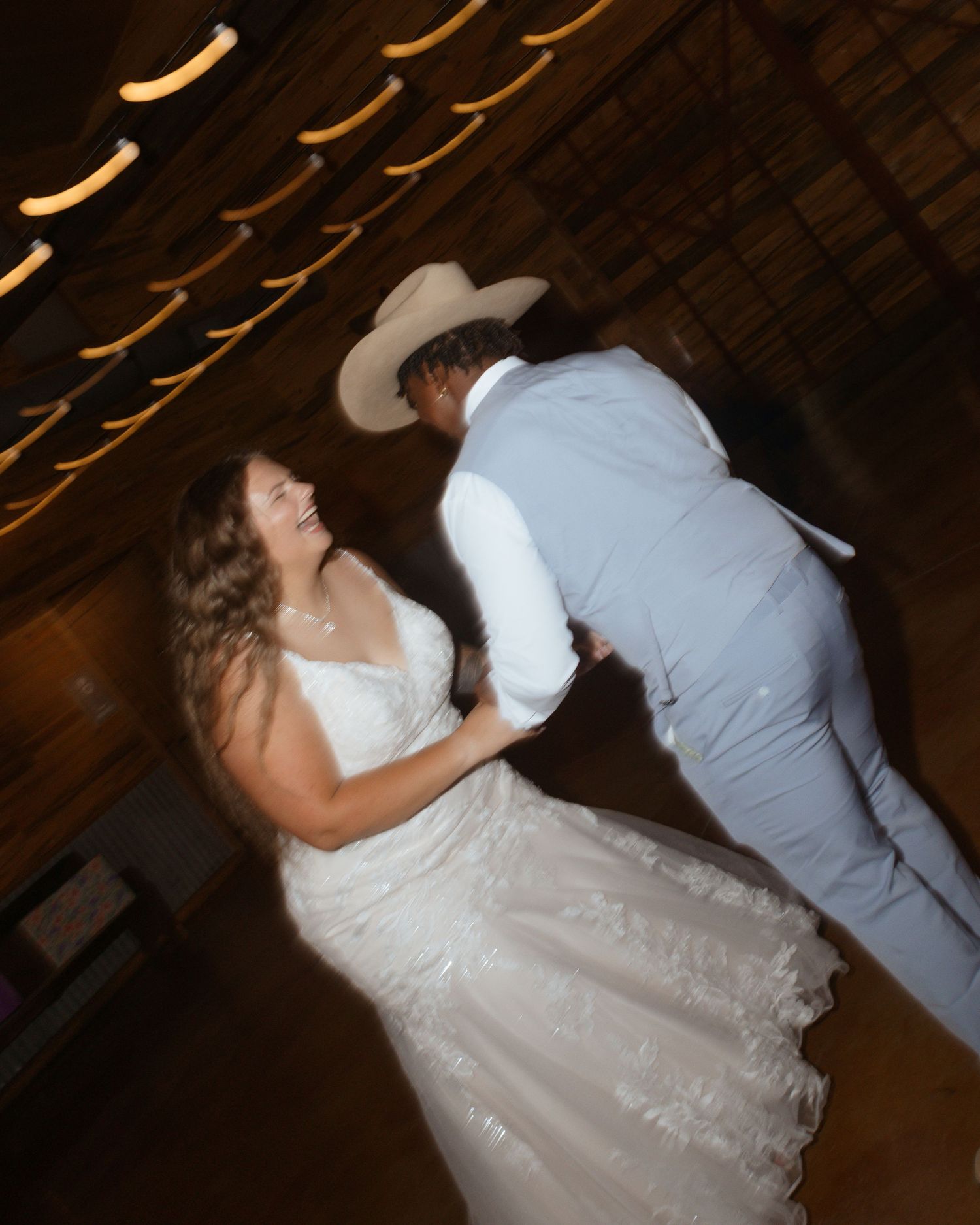 Bride and groom sharing joyful first dance in rustic barn venue with string lights overhead.