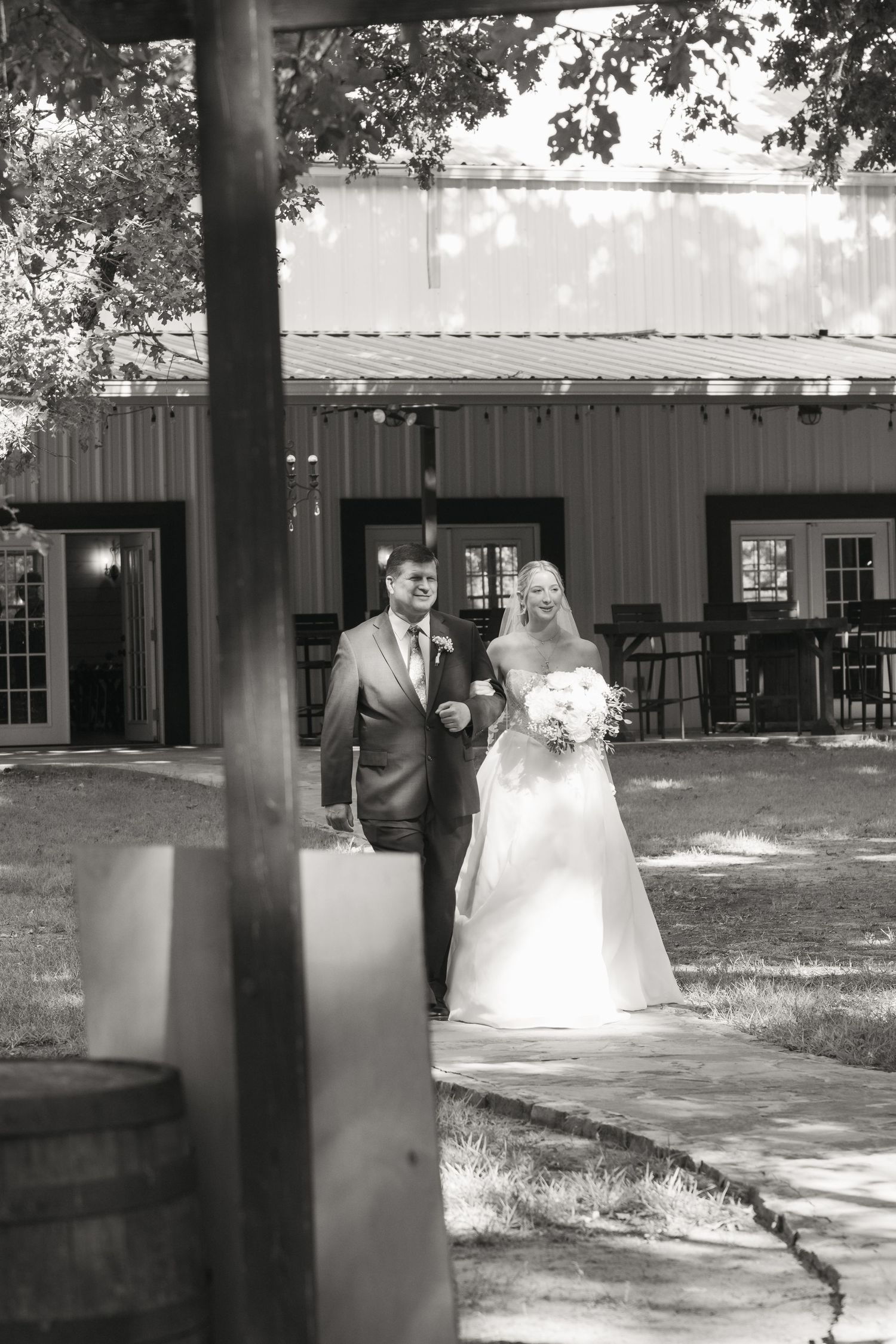 Black and white photo of a bride and groom walking together outside a rustic barn venue on their wedding day.