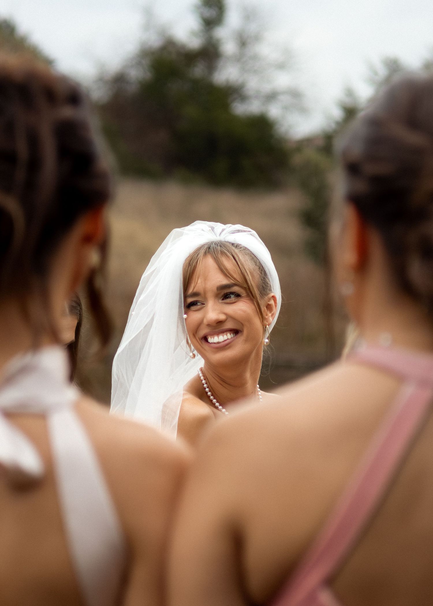A bride shares a joyful moment with bridesmaids in pink dresses during an outdoor wedding celebration.