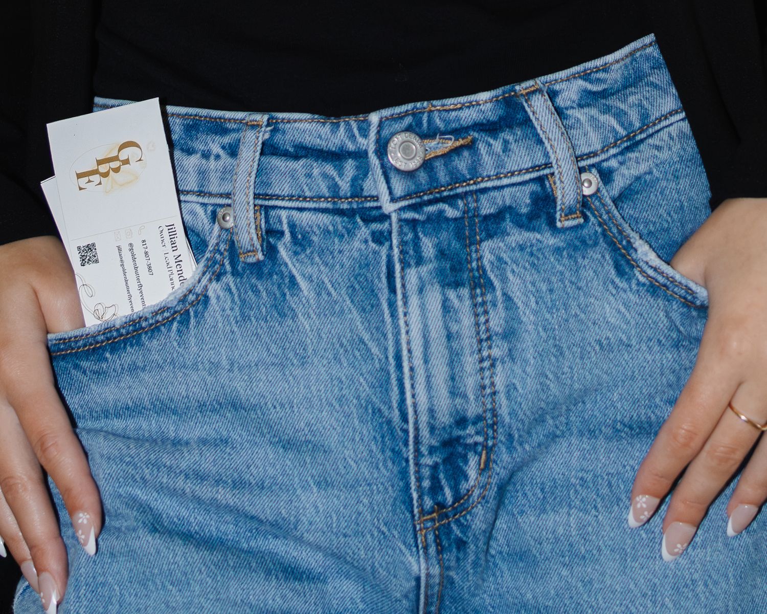 Close-up of blue denim jeans with a gold logo business card tucked into the front pocket.