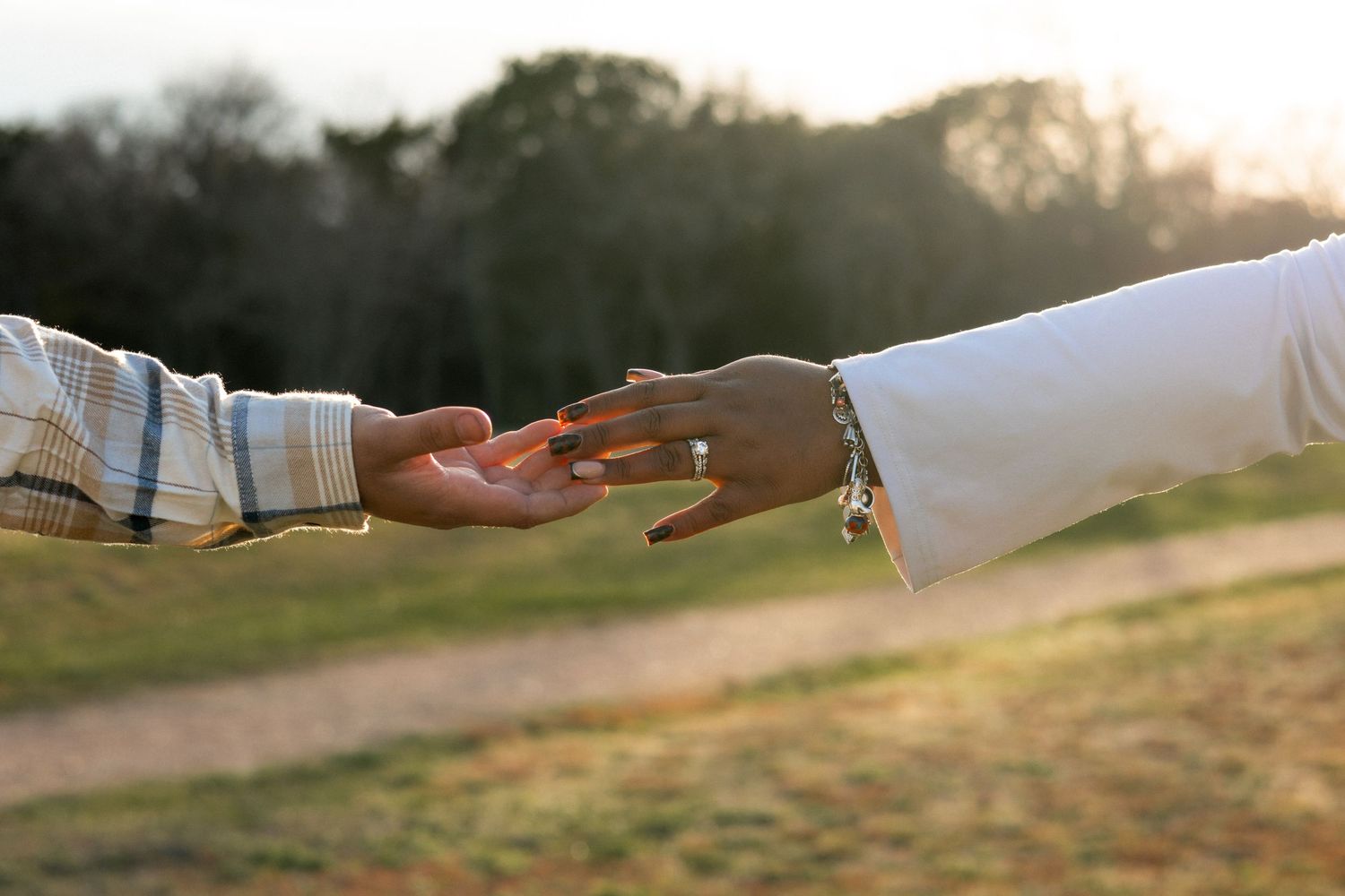 Hands reaching out towards each other against a blurred outdoor background at sunset.
