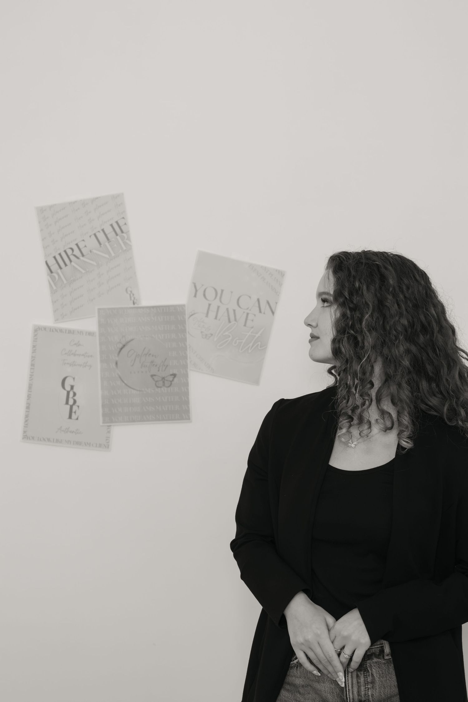 Black and white portrait of a curly-haired woman standing beside motivational wall prints.