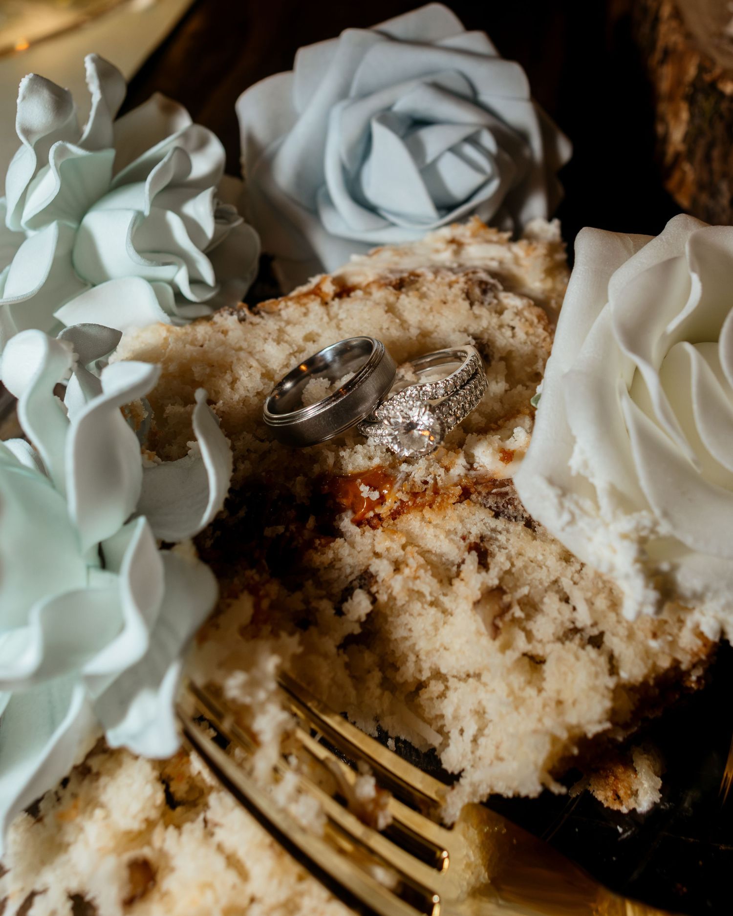 Wedding rings resting on a slice of cake surrounded by white and blue roses.