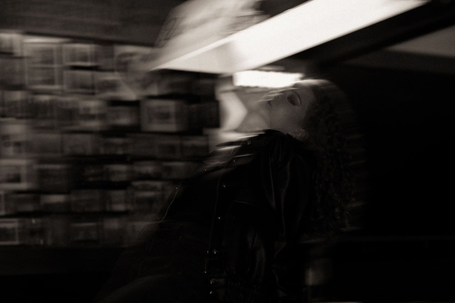 Blurred black and white photo of a person in a dark jacket under dramatic lighting with motion blur effect.