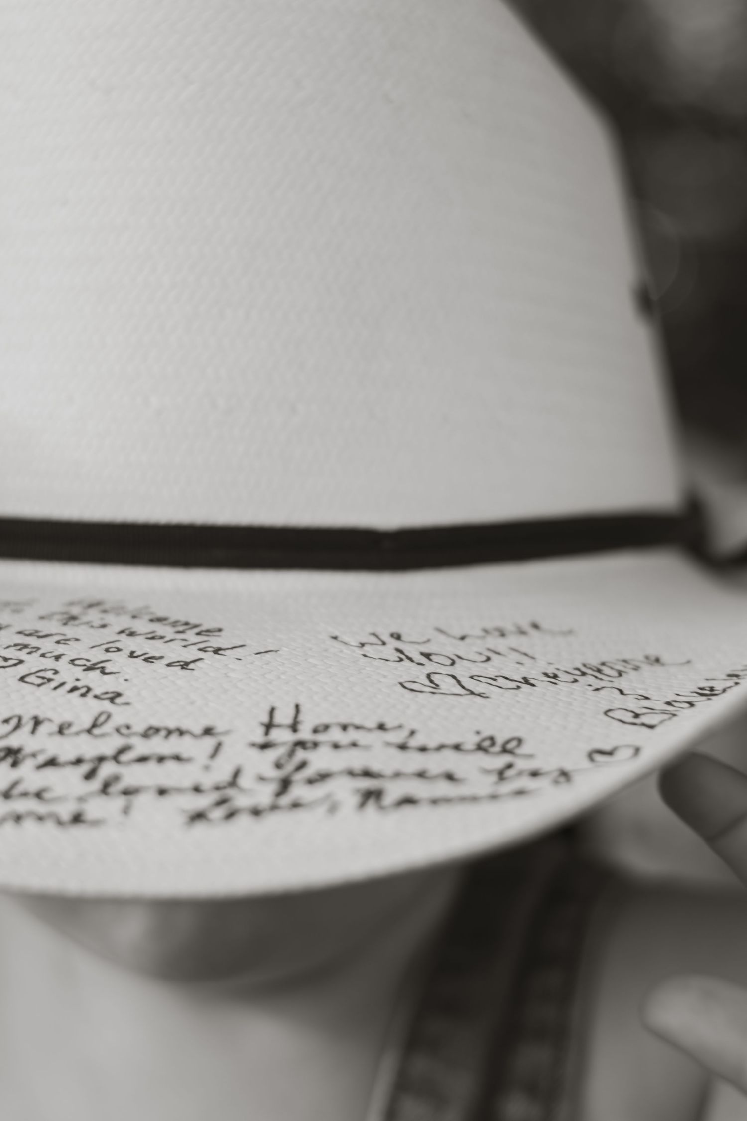 Black and white photo of a white hat with handwritten messages including Welcome Home on the brim.