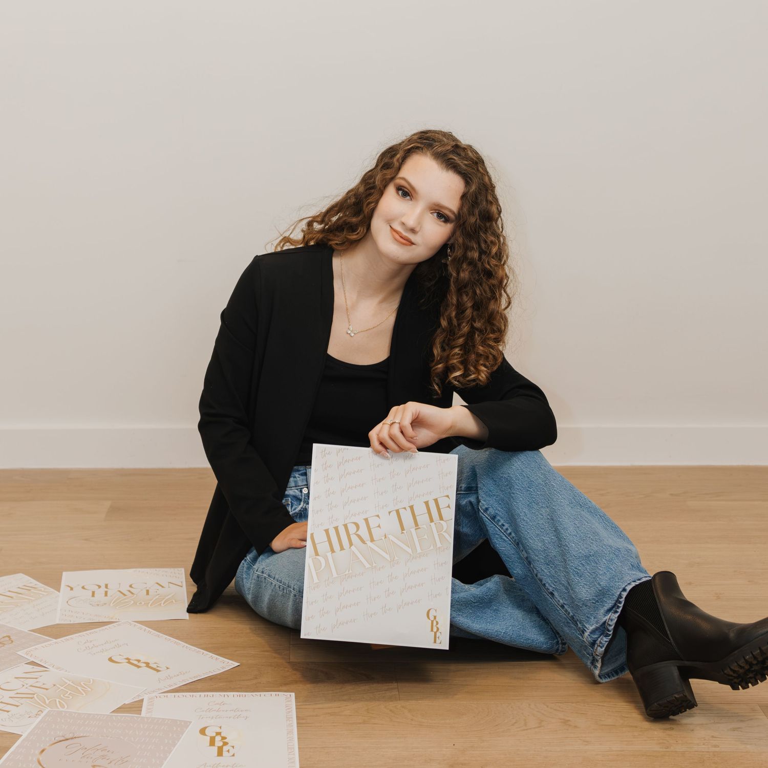 Smiling young woman in black blazer sitting on floor holding 