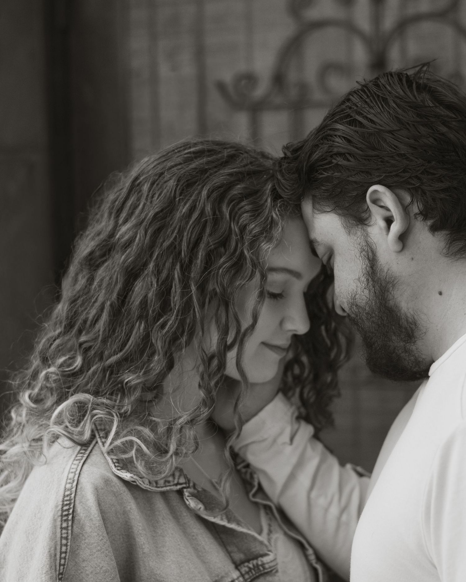 Intimate black and white portrait of a couple in a tender moment, with her curly hair and denim jacket visible.
