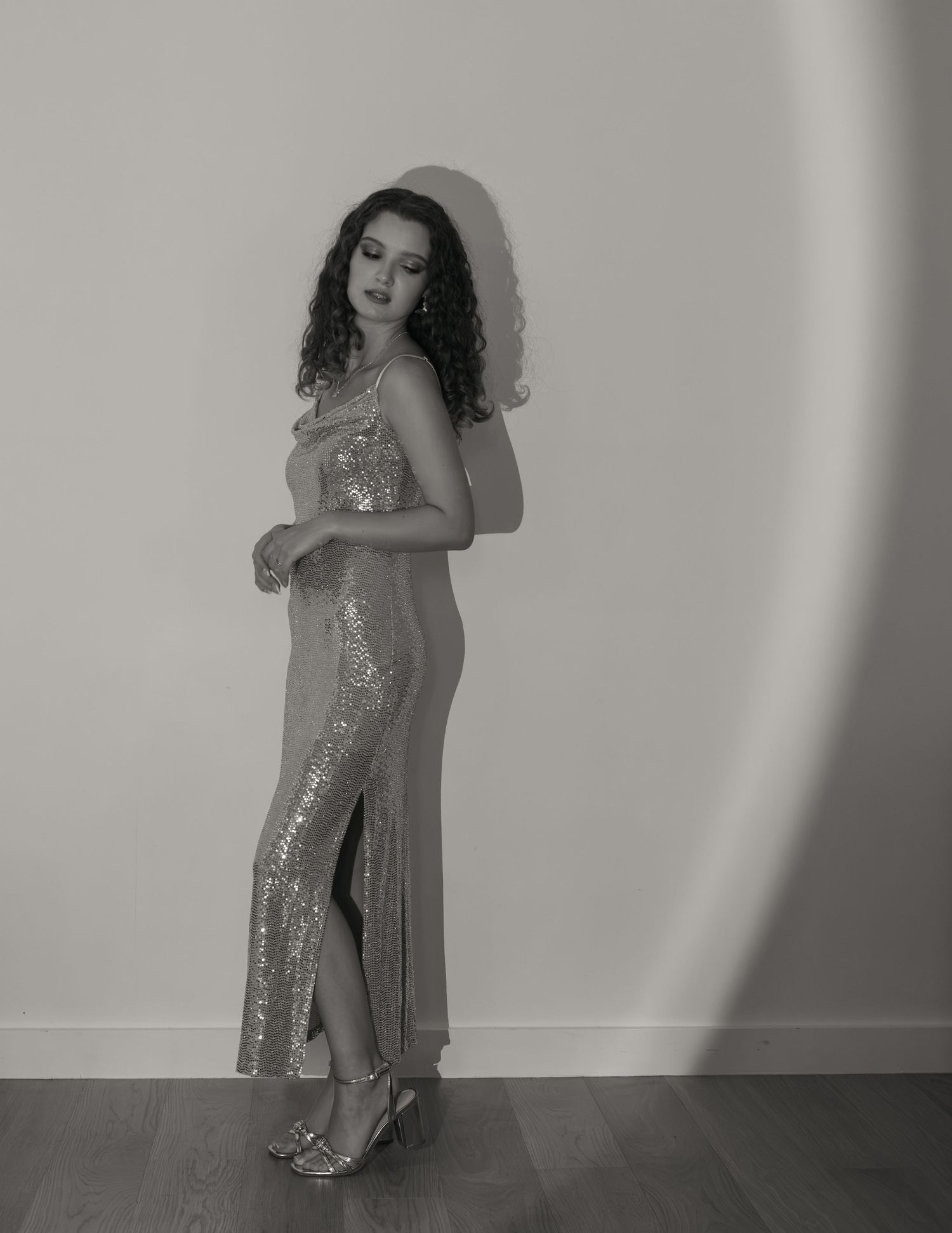 Woman in gold sequin gown posing elegantly in black and white portrait photography.