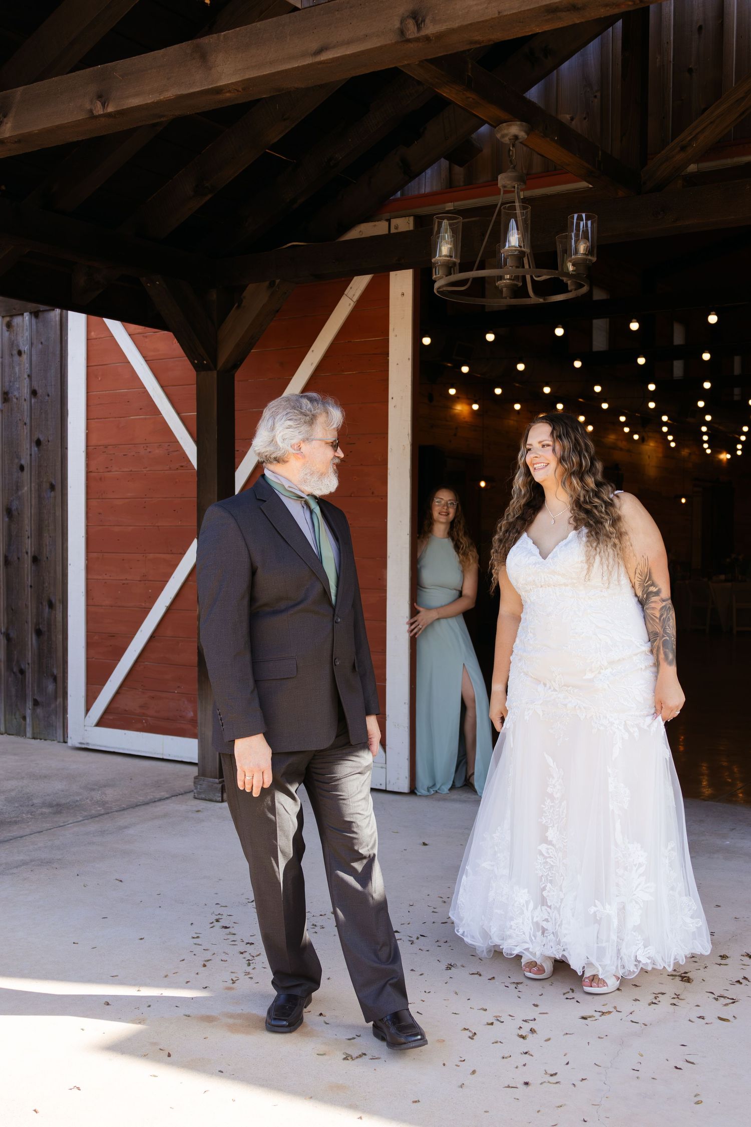 Bride in lace wedding gown shares a first look moment with her father inside a rustic barn wedding venue.